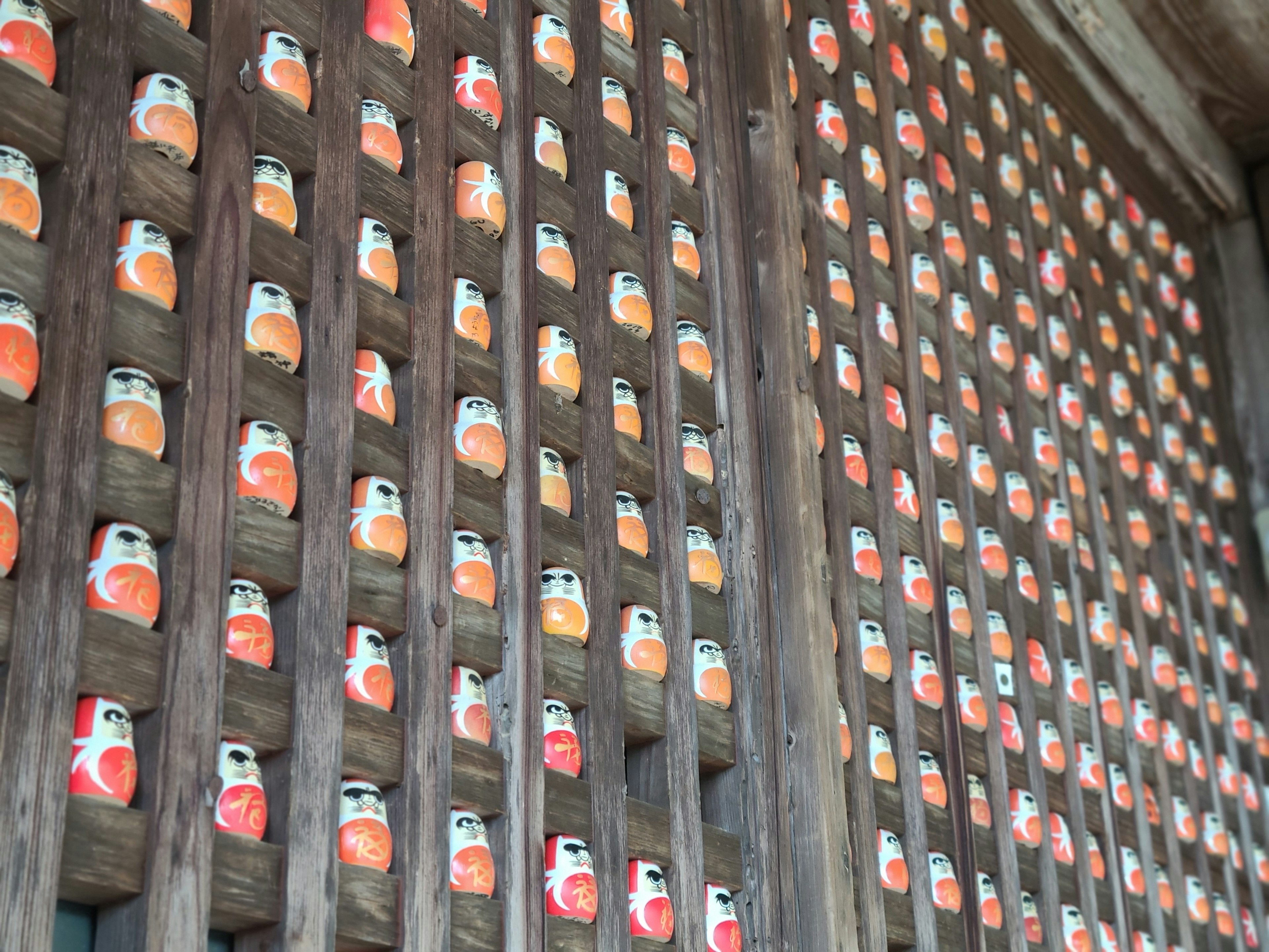 Muñecas Daruma coloridas dispuestas en una rejilla de madera