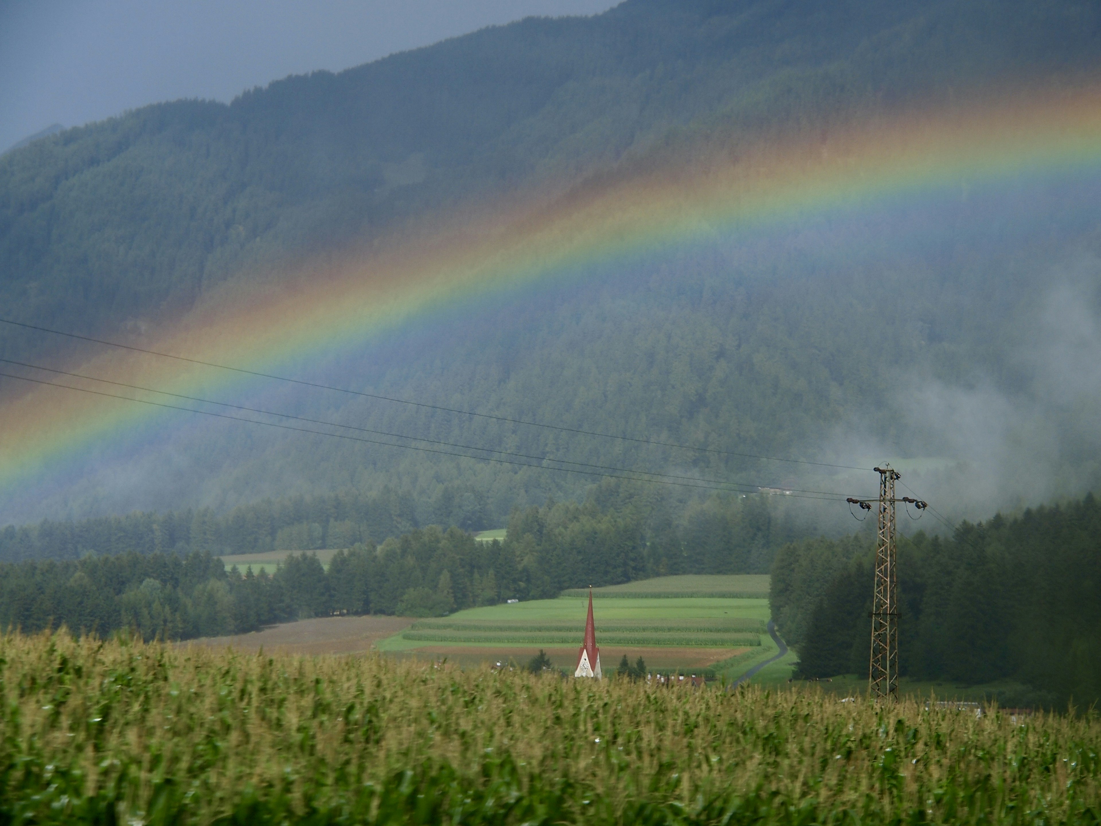 Arc-en-ciel au-dessus des montagnes avec des champs verdoyants et un clocher