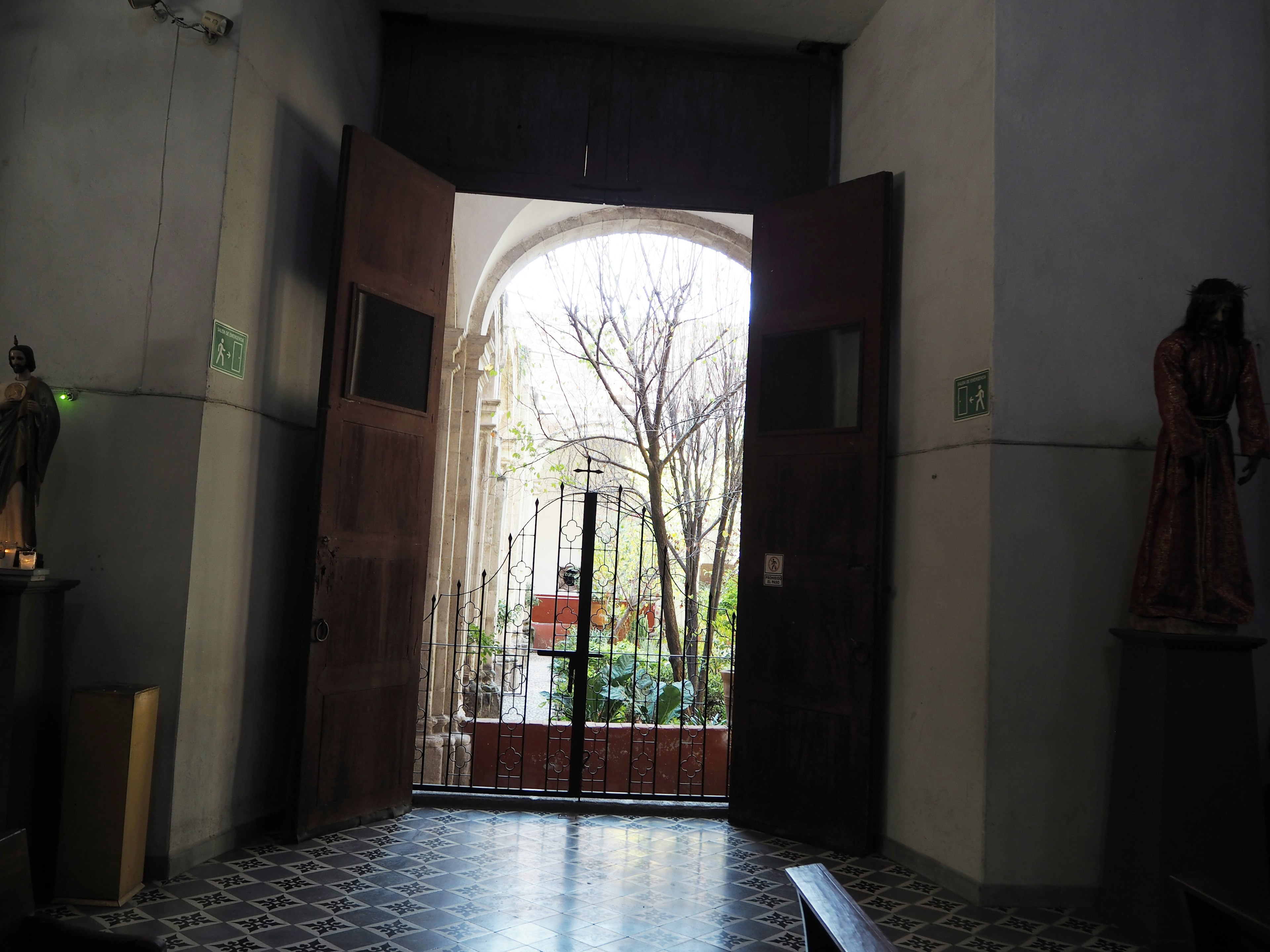 Interior view of a church with large wooden doors open revealing trees outside