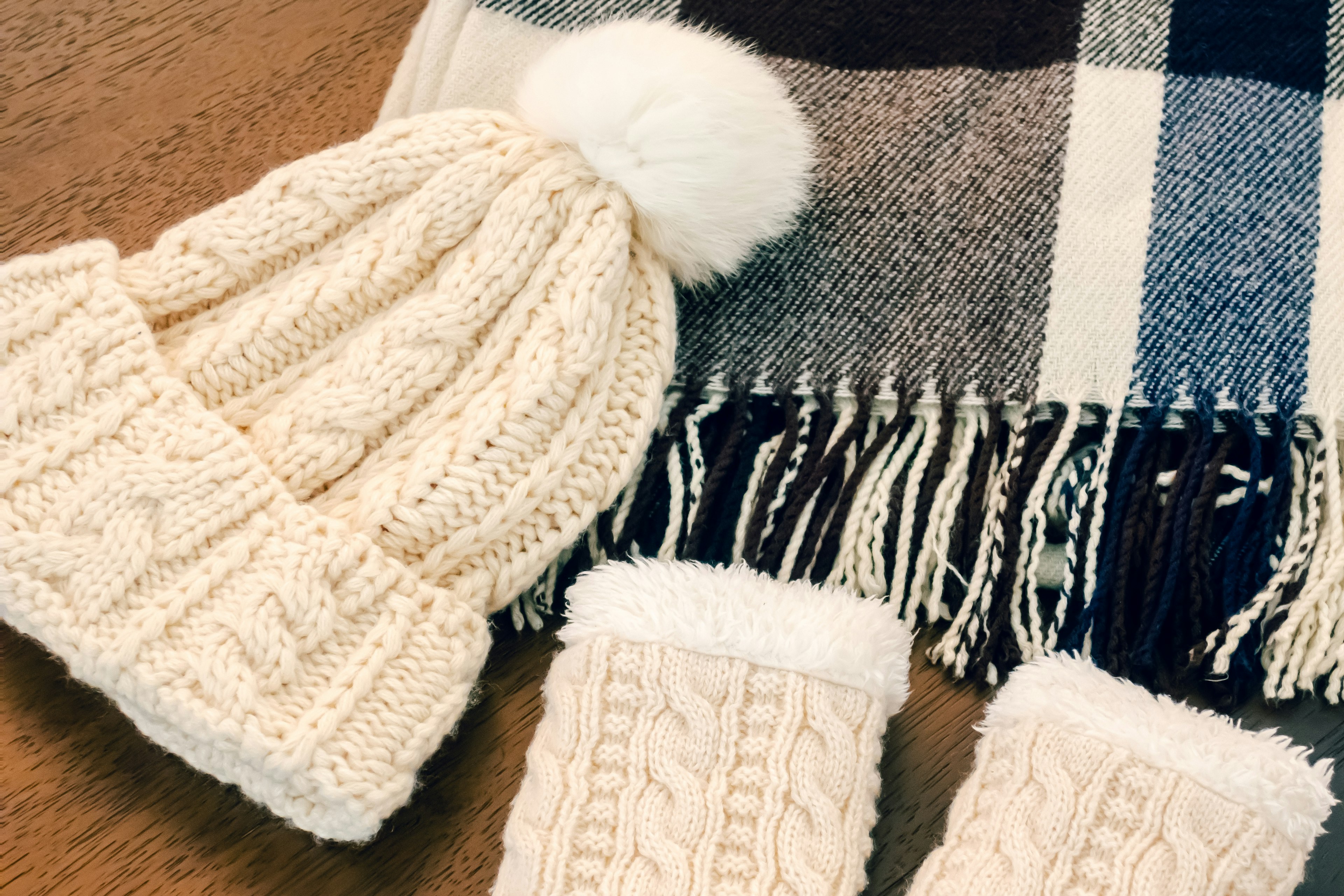 Cream knitted beanie with pom-pom and matching mittens alongside a plaid scarf