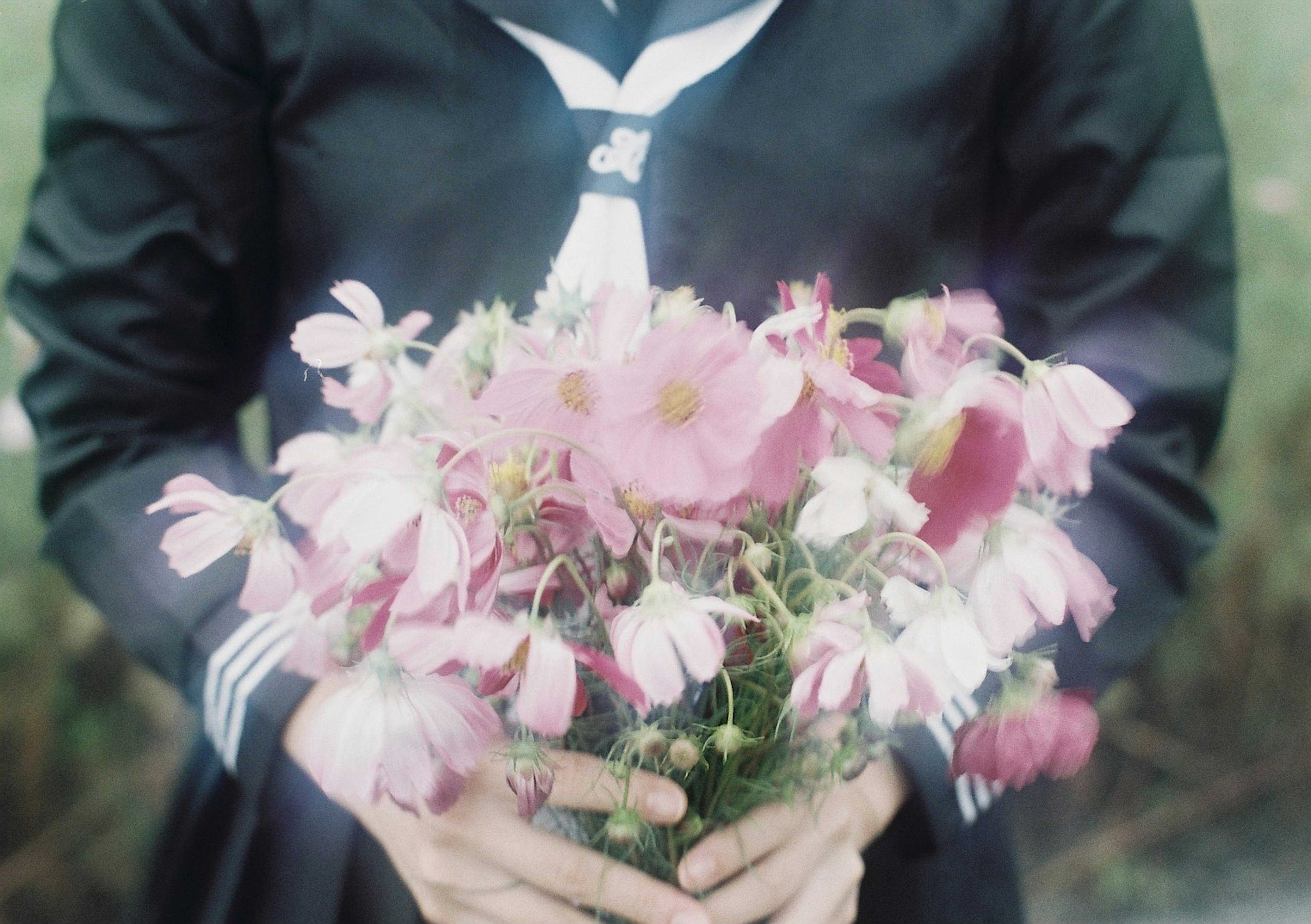 Person in schwarzer Uniform hält einen Strauß pinker Blumen