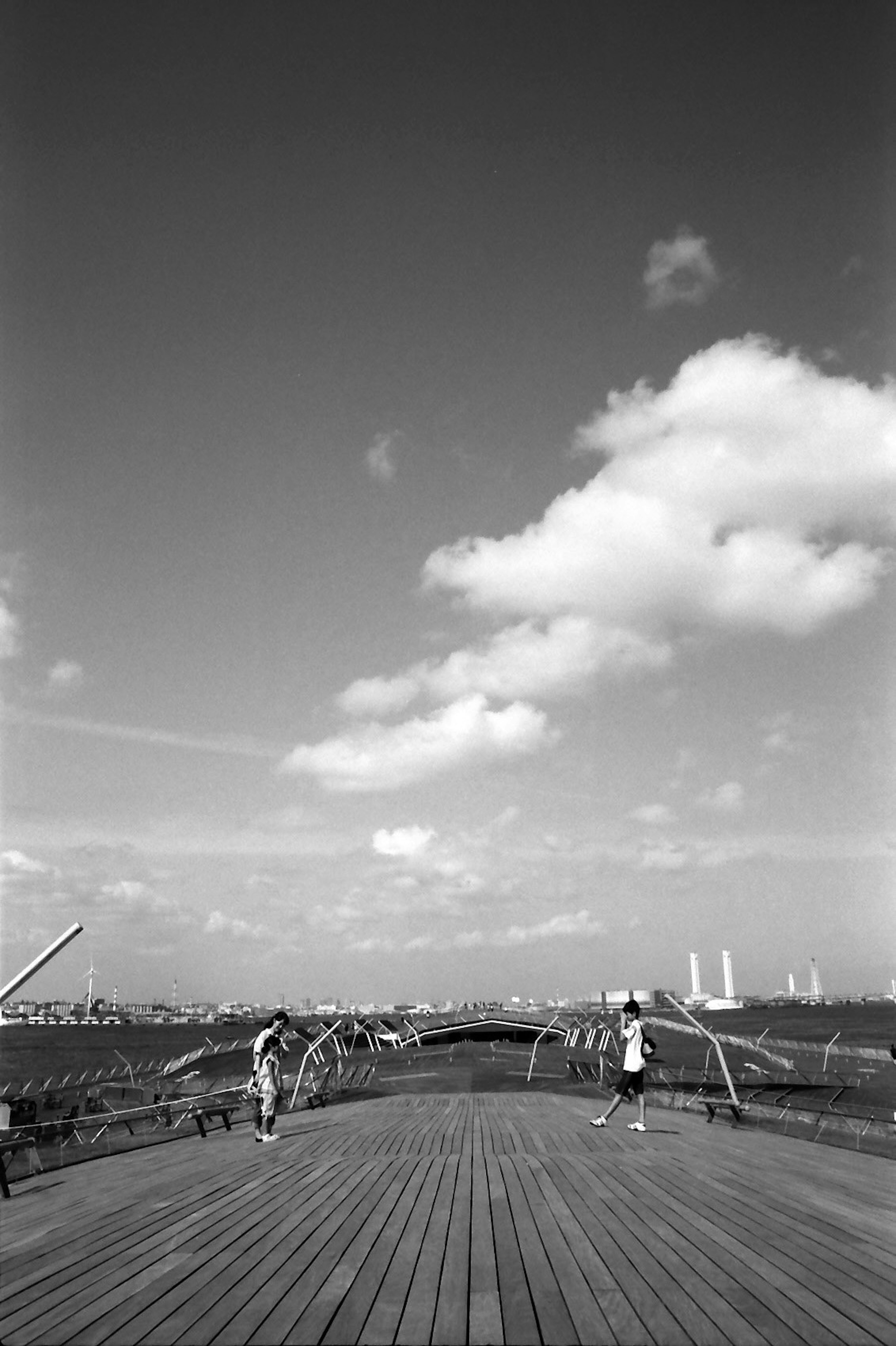 Schwarz-weiß Landschaft mit Menschen auf einem Holzdeck einer Brücke unter blauem Himmel