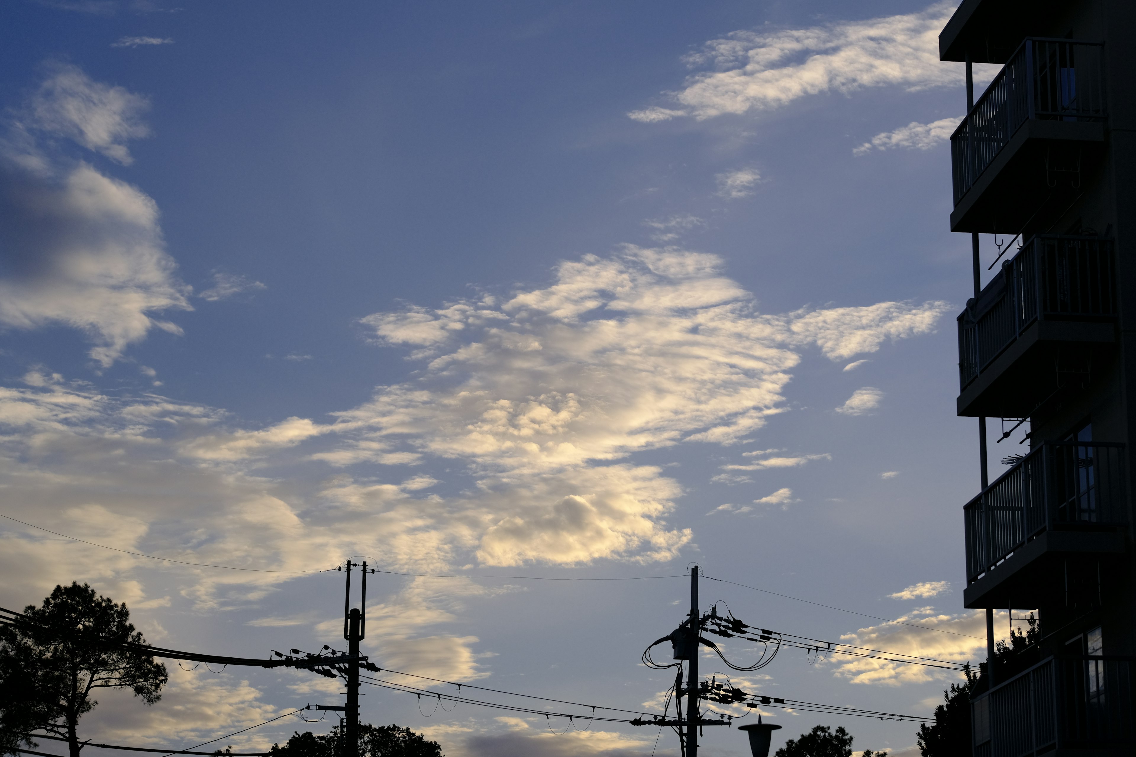 Pemandangan langit biru dengan awan menampilkan bangunan dan kabel listrik