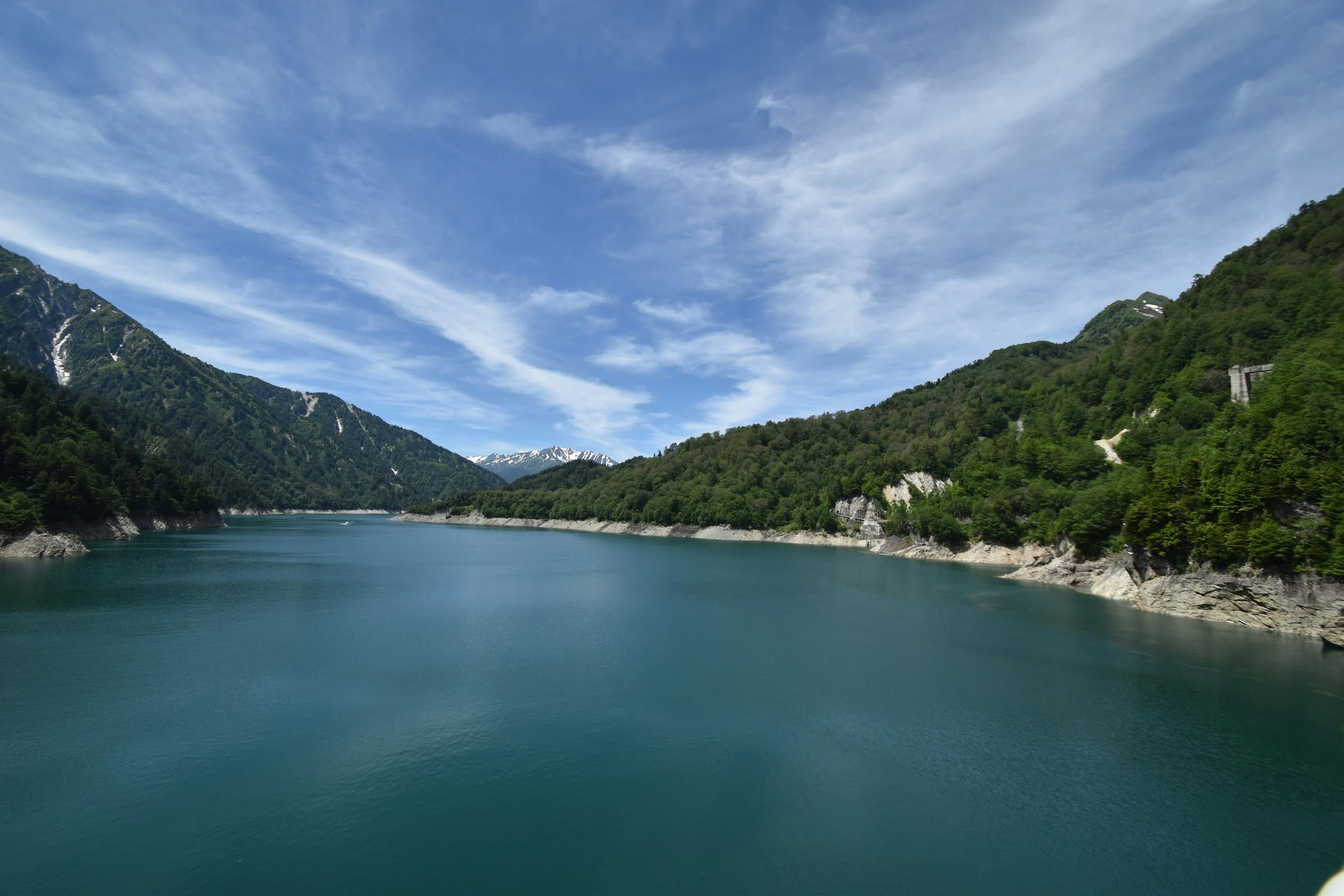 Scenic lake surrounded by green mountains under a blue sky with white clouds