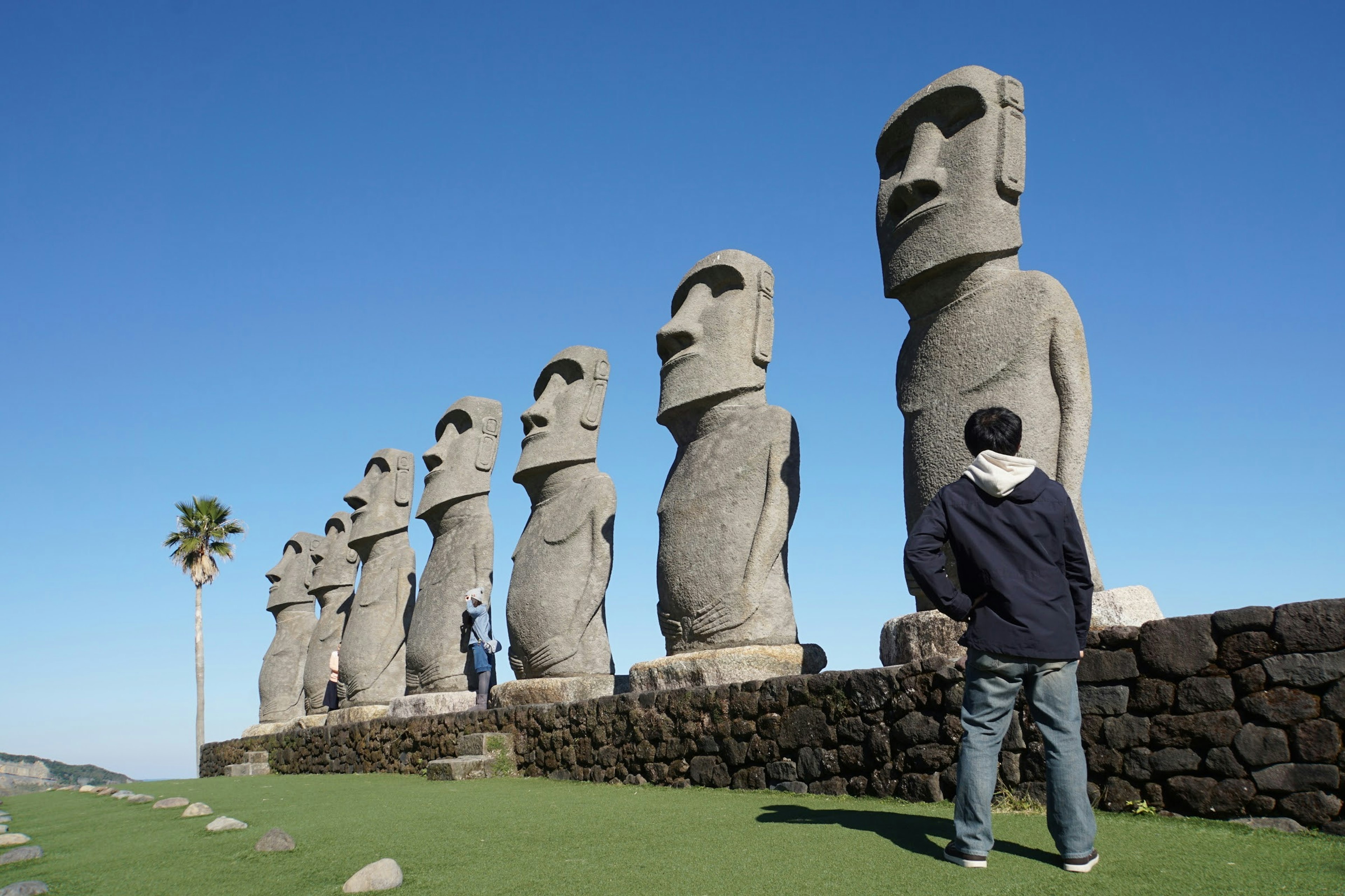 Ligne de statues Moai avec un visiteur à proximité