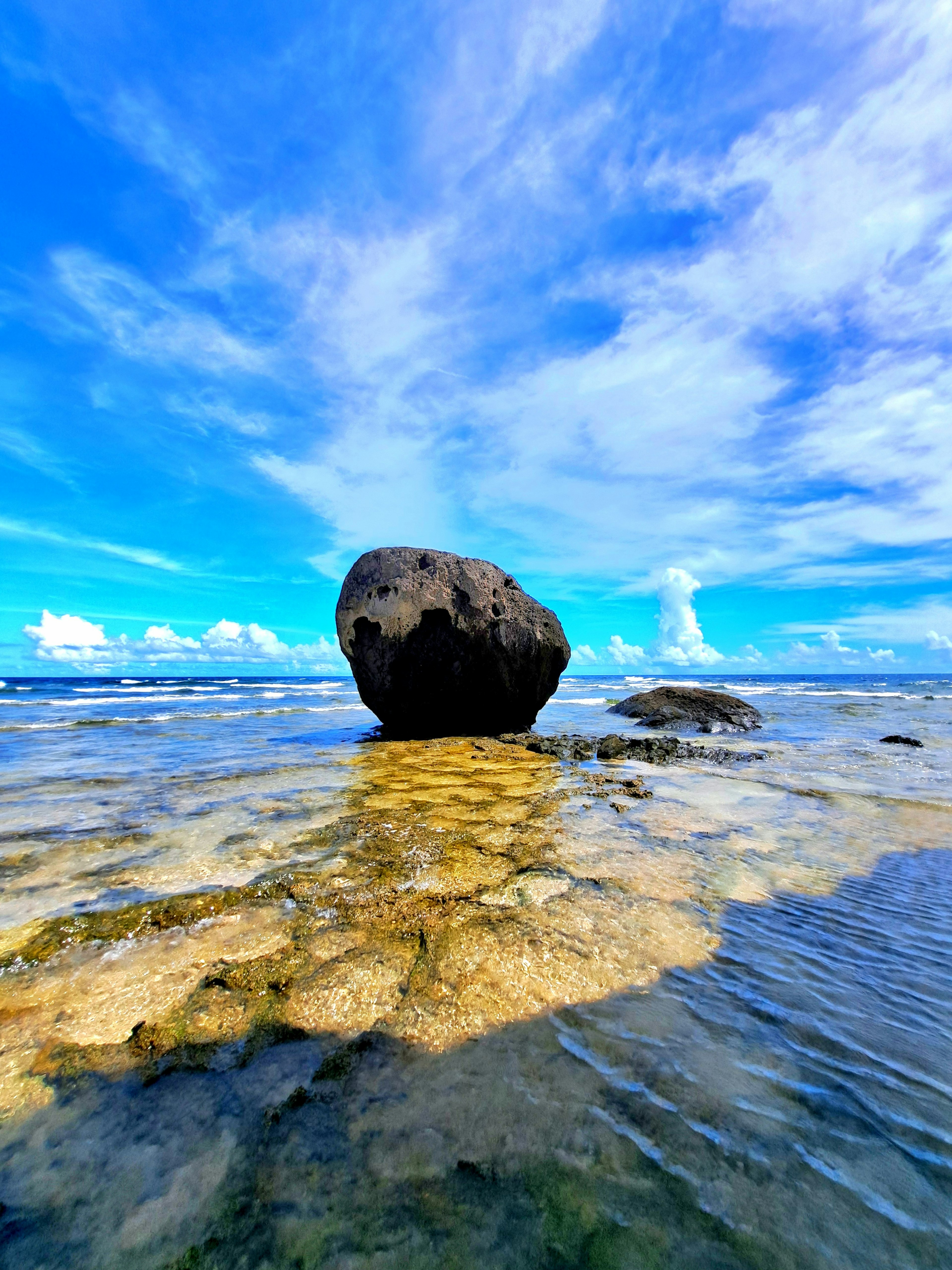 Una grande roccia nell'acqua bassa sotto un cielo blu brillante