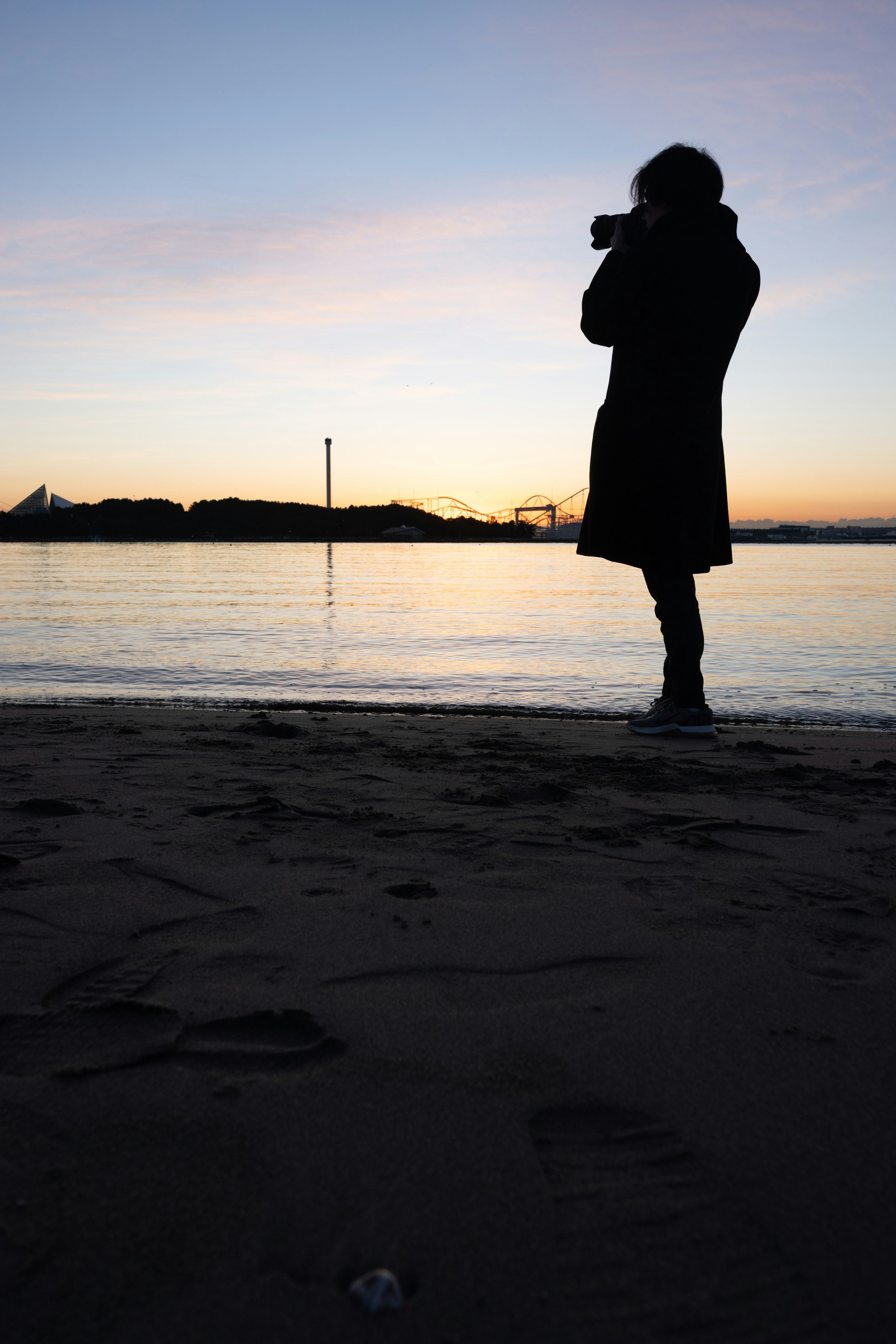 海岸でカメラを持つシルエットの人物と夕焼けの風景