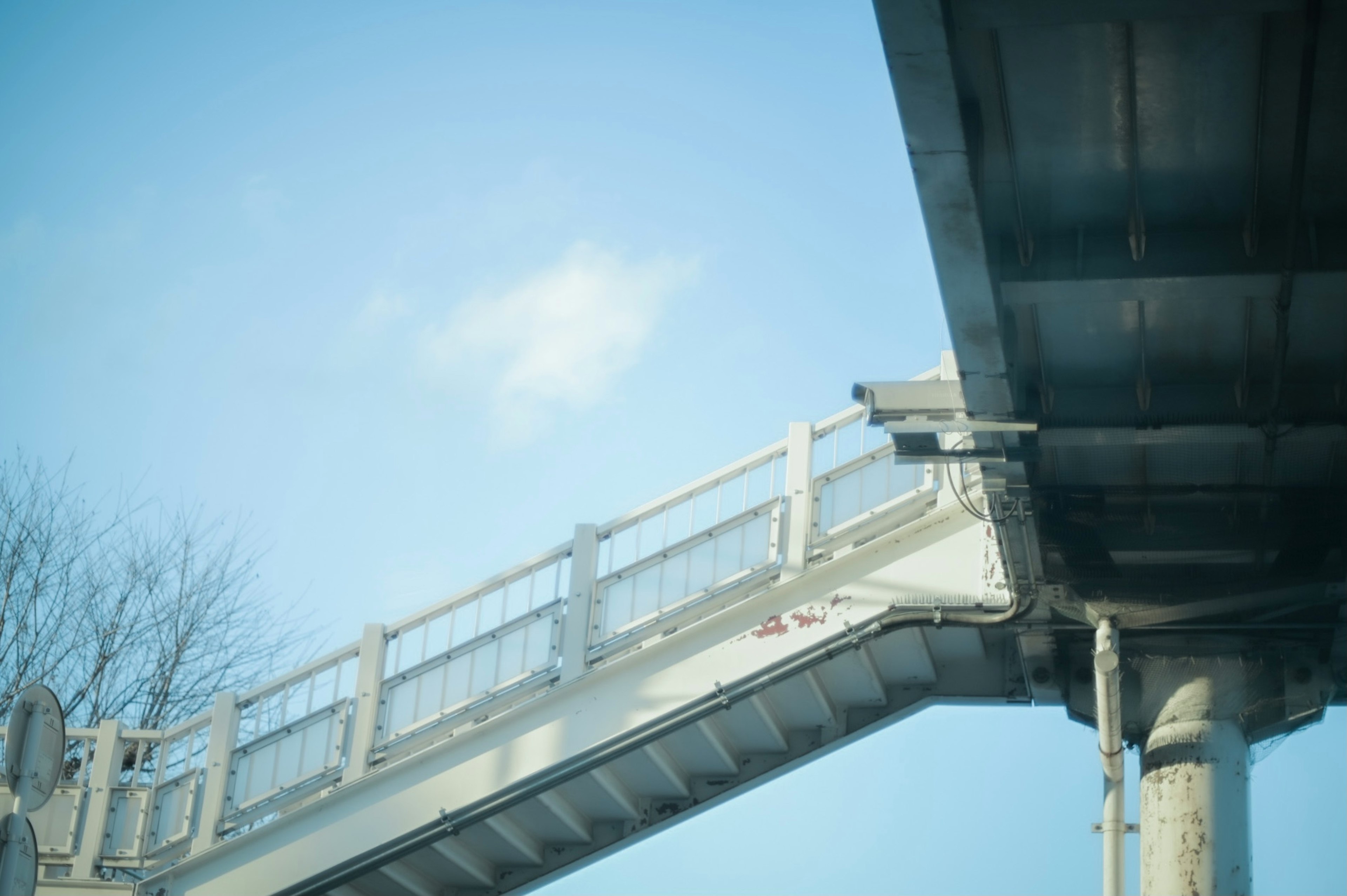 青空の下にある白い歩道橋の一部とその接続部