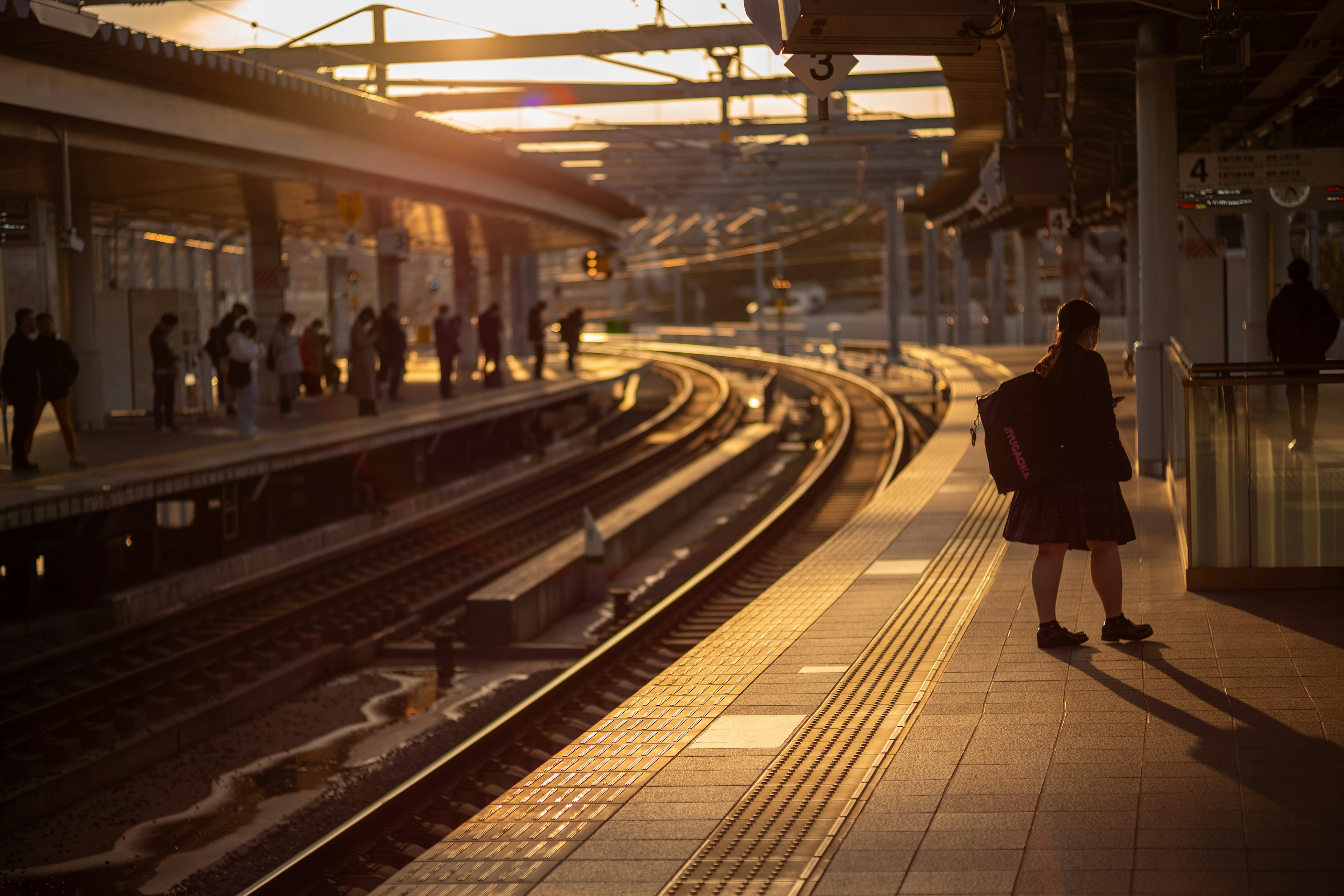 Personas esperando en una estación de tren al atardecer con vías curvas