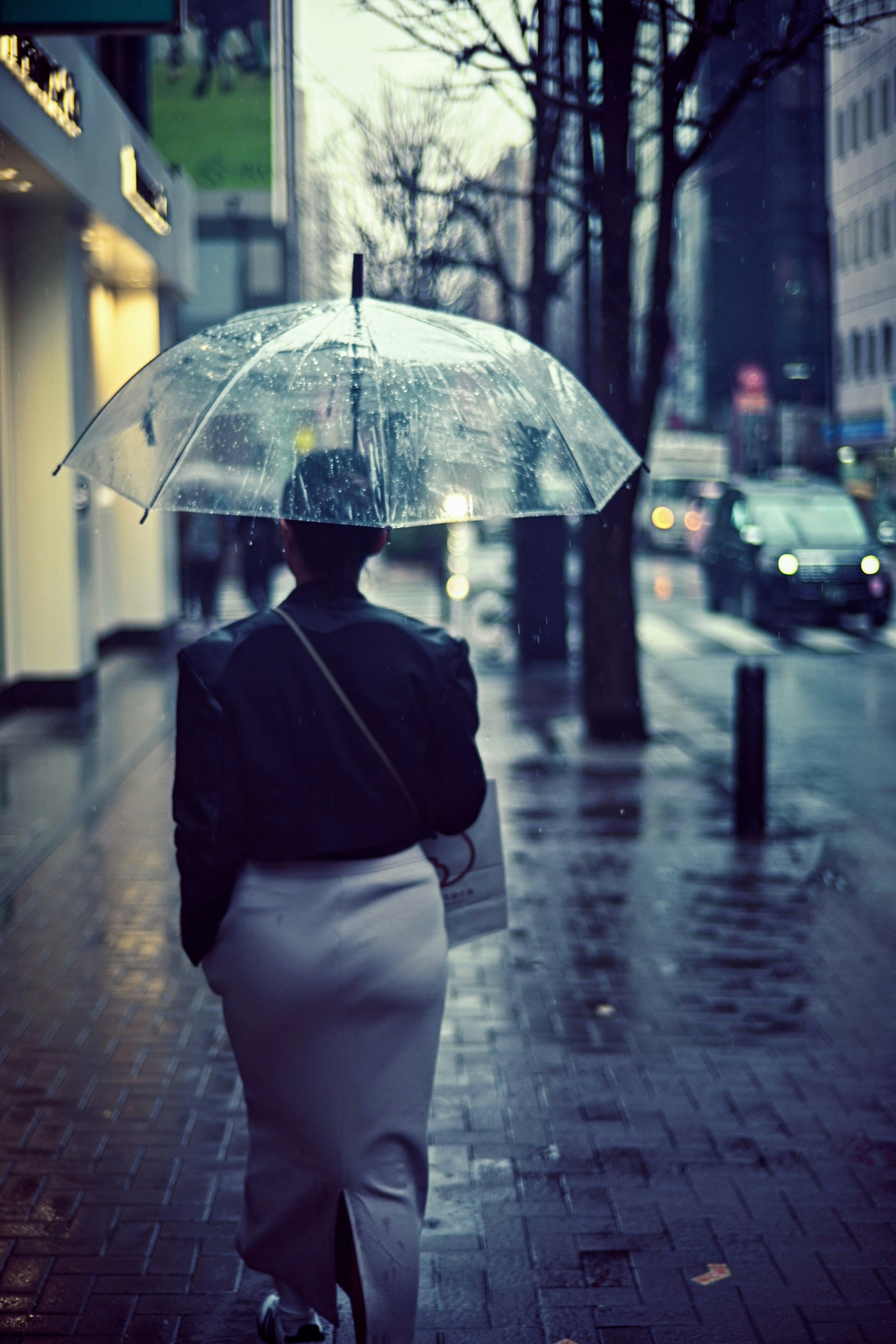 Une femme marchant sous la pluie avec un parapluie transparent dans un cadre urbain