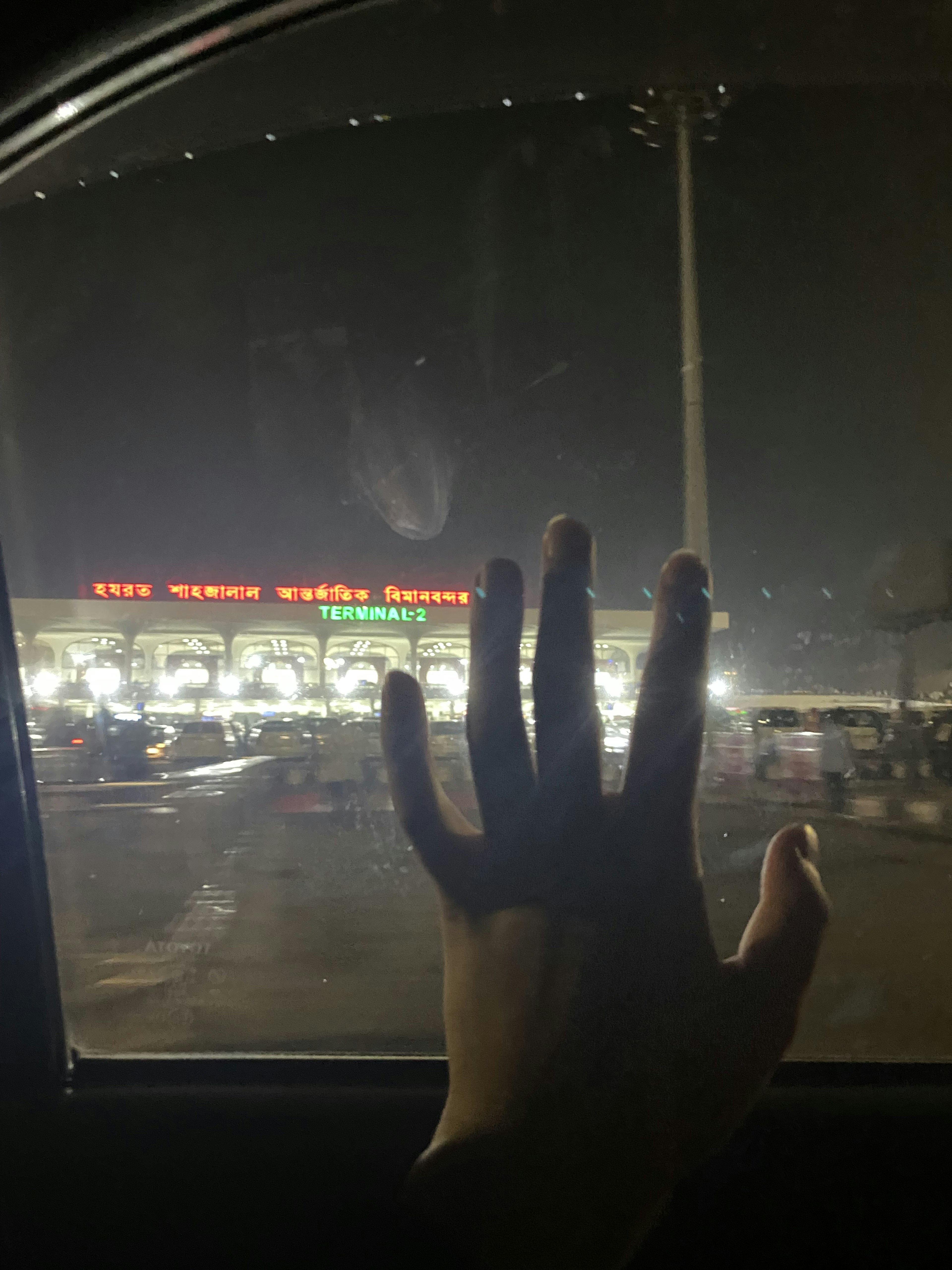 Silhouette of a hand reaching out through a car window at night with bright signage in the background