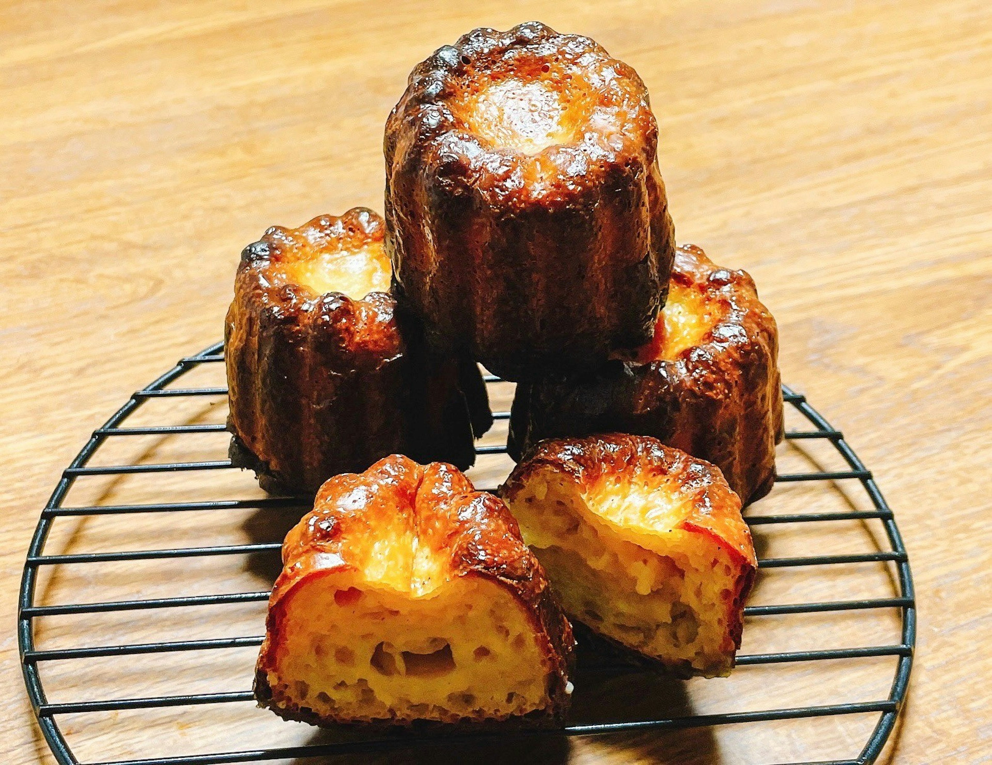 Gambar kue canelé di rak kawat yang menunjukkan bagian luar karamel dan bagian dalam yang lembut