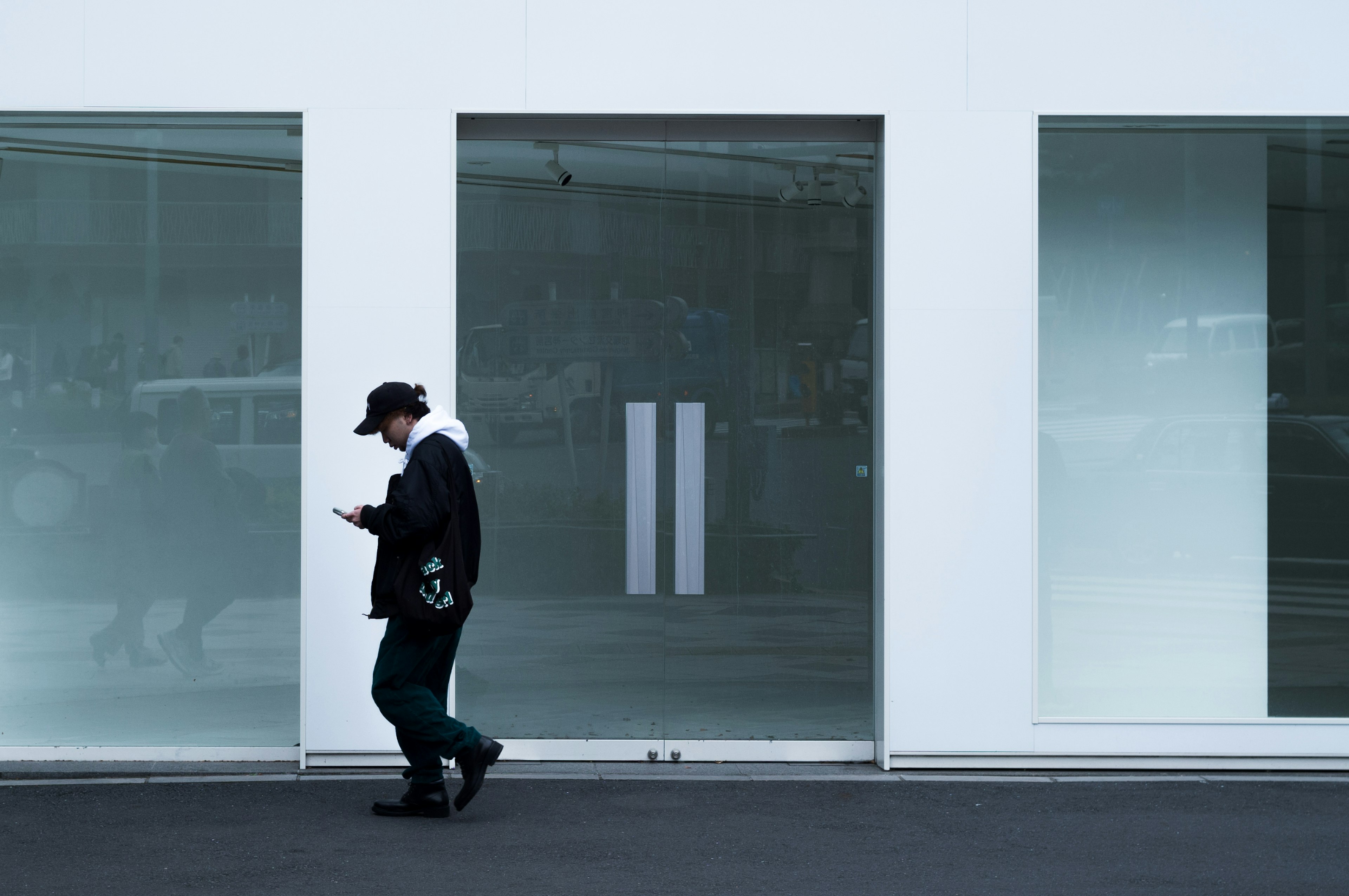 Un hombre caminando frente a una pared blanca mirando su smartphone