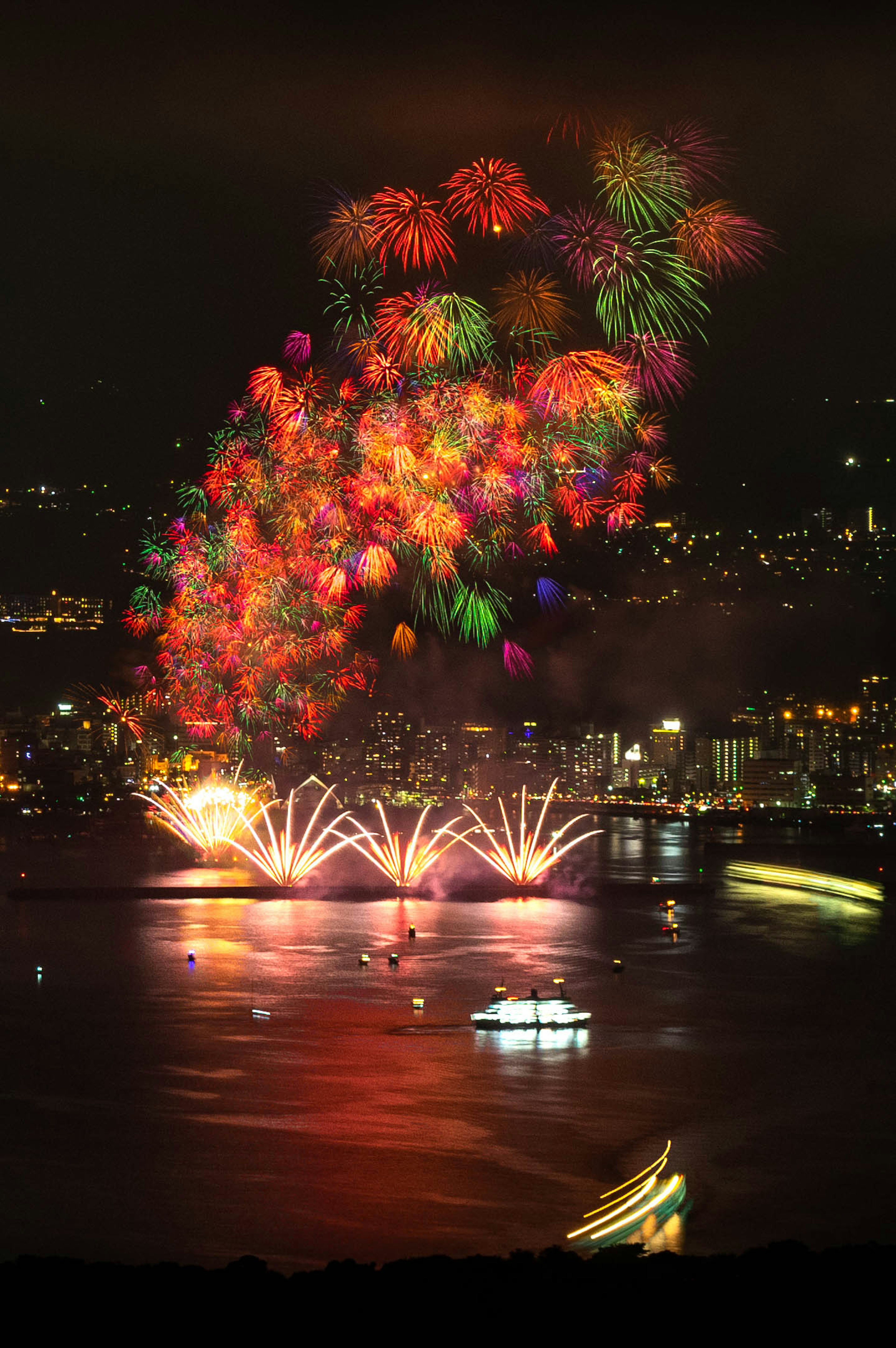 Fuochi d'artificio colorati che esplodono nel cielo notturno con riflessi sull'acqua