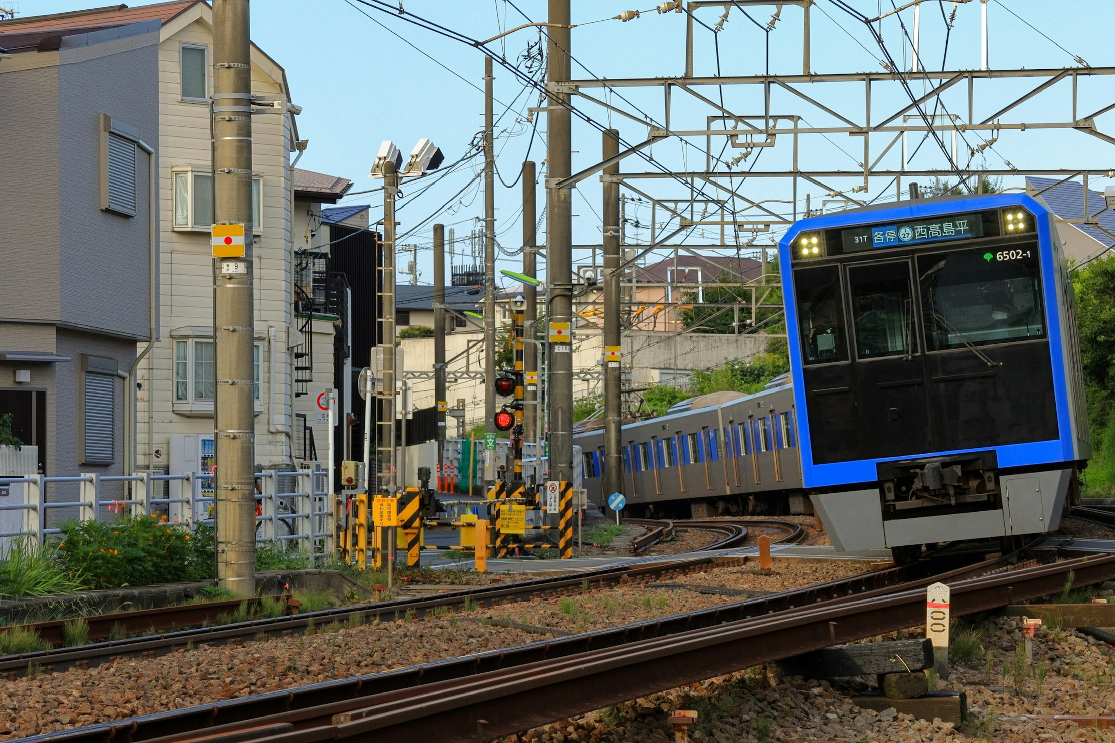 A blue train passing through a railway scene with nearby buildings and utility poles