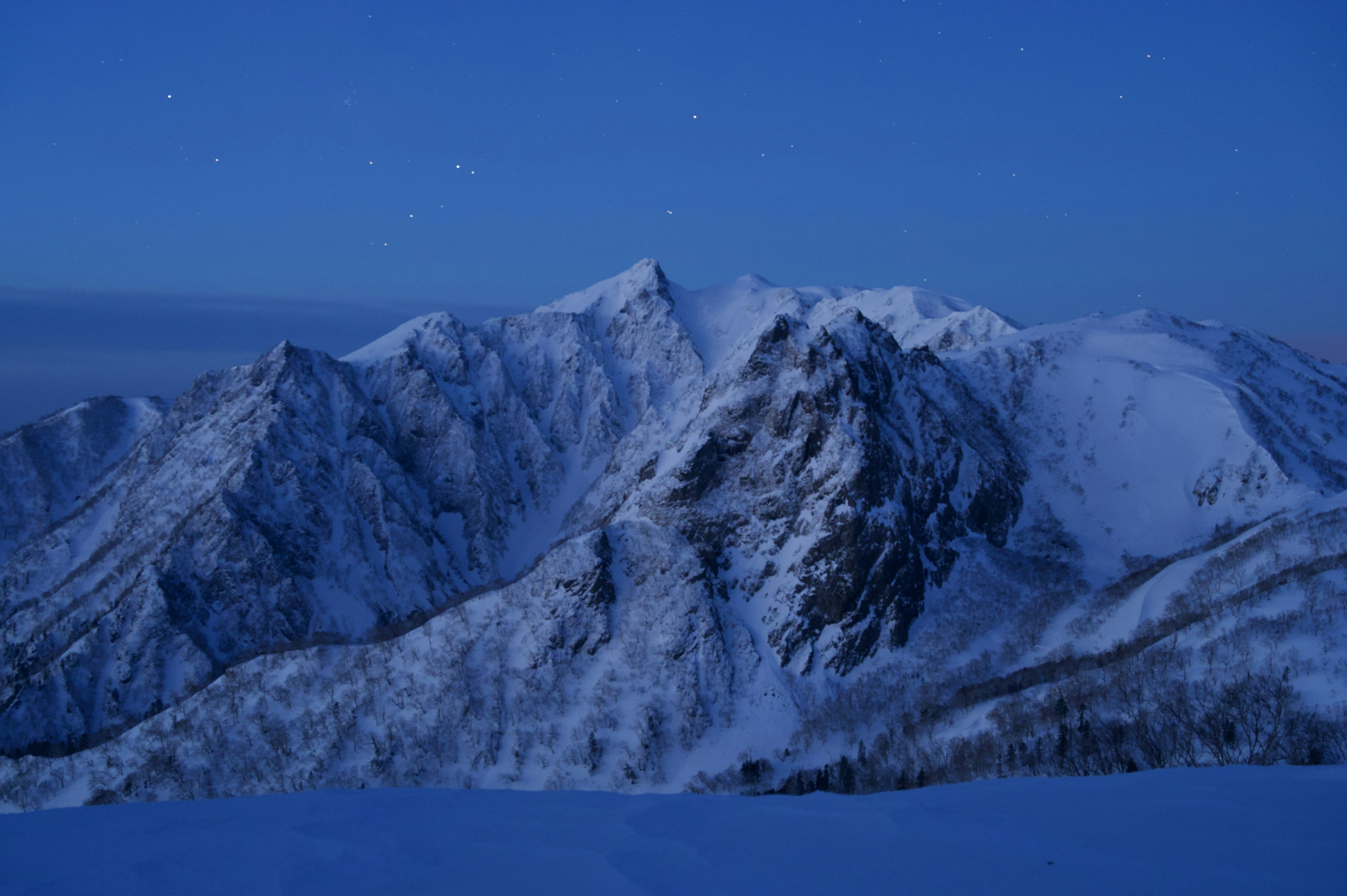 青い夜空の下にそびえる雪に覆われた山々の風景