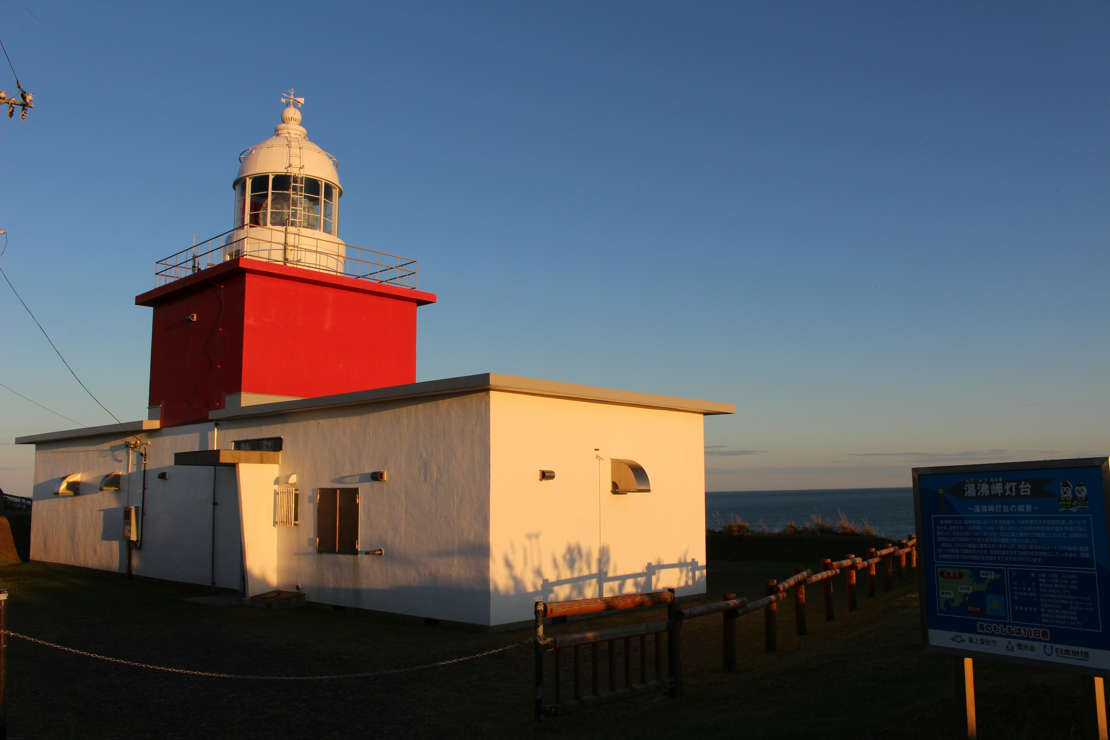 Red lighthouse with white building against ocean backdrop