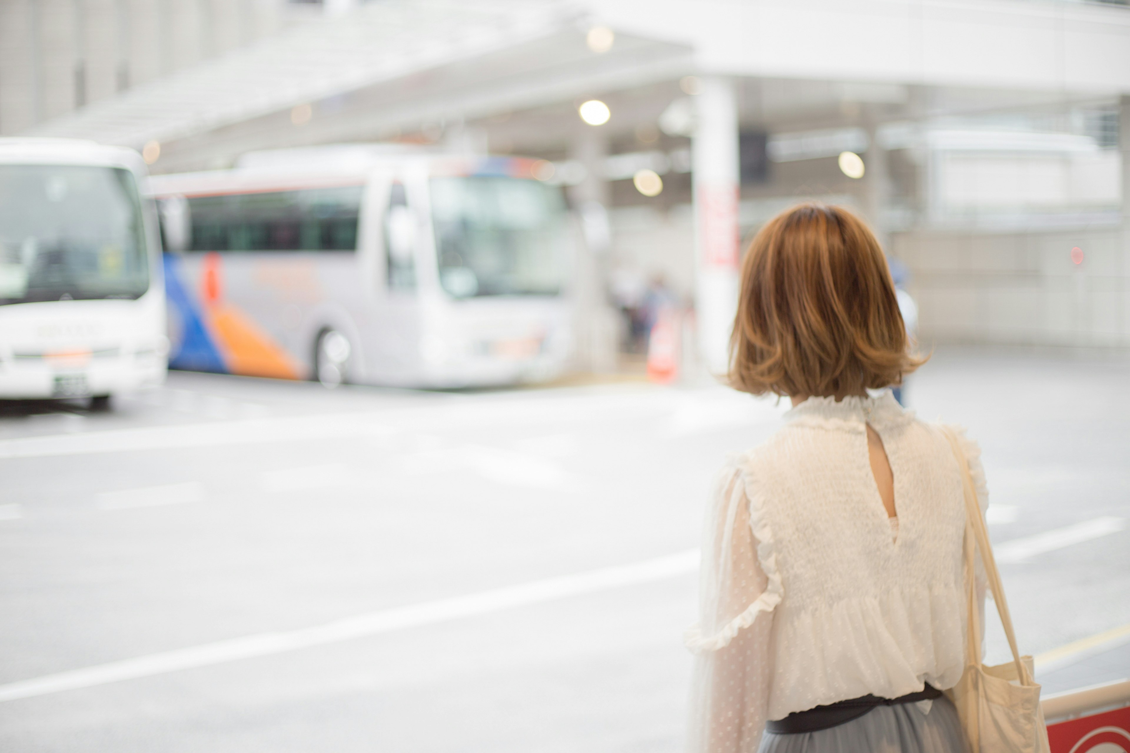 A woman waiting at a bus stop with buses in the background