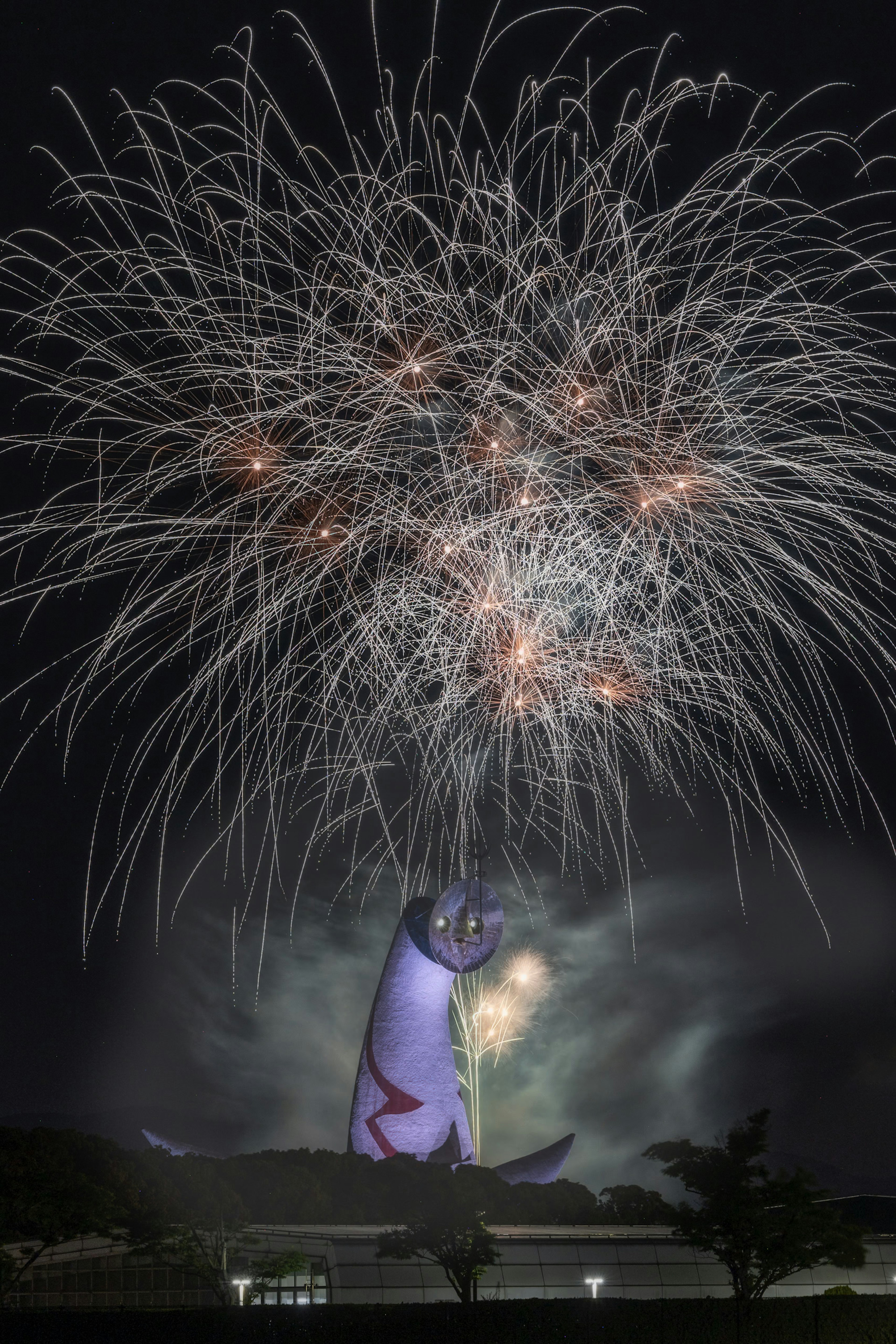 夜空に花火が打ち上げられその下に大きな猫の像があるシーン