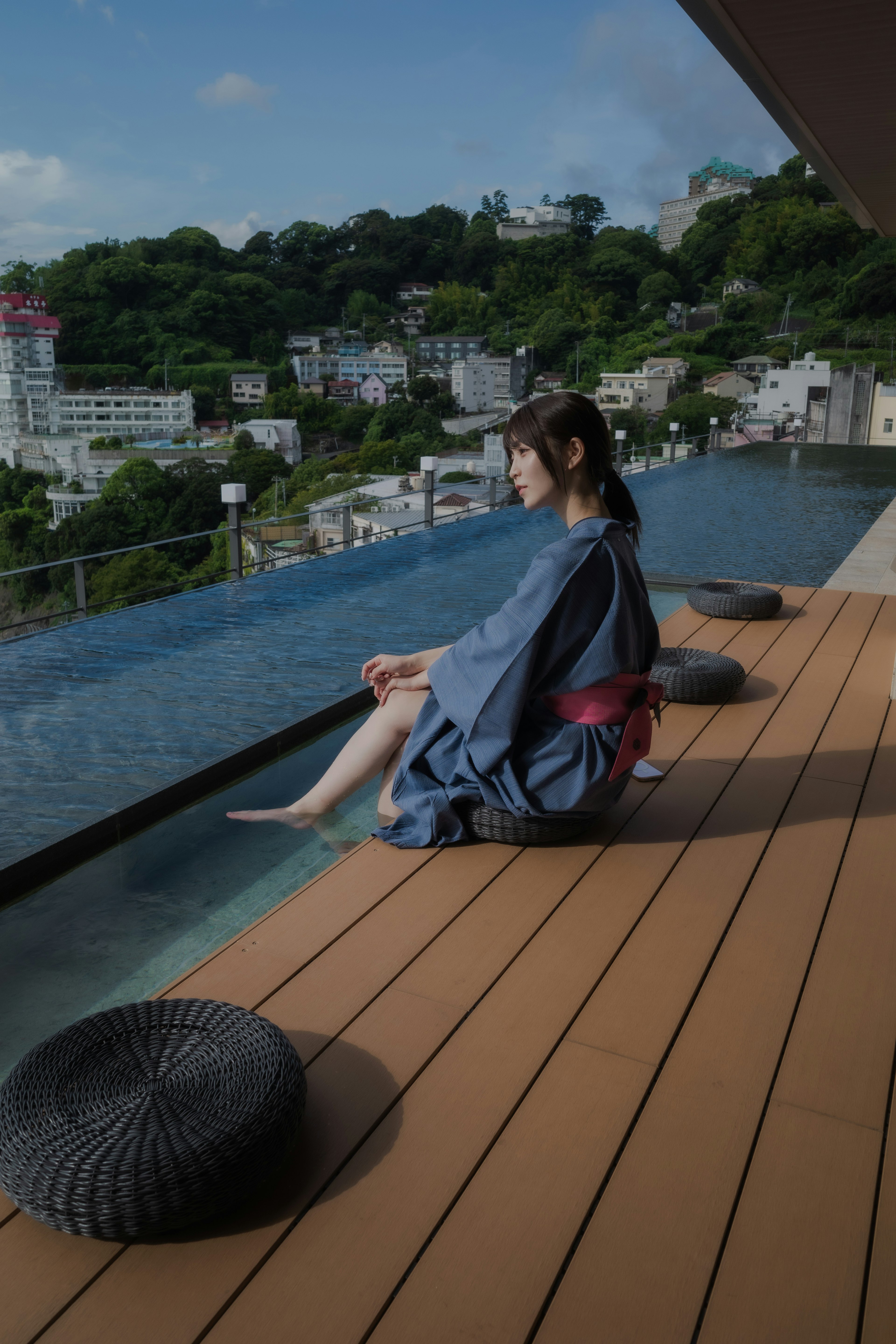 Perempuan berpakaian yukata tradisional bersantai di tepi kolam renang luar ruangan dengan pemandangan