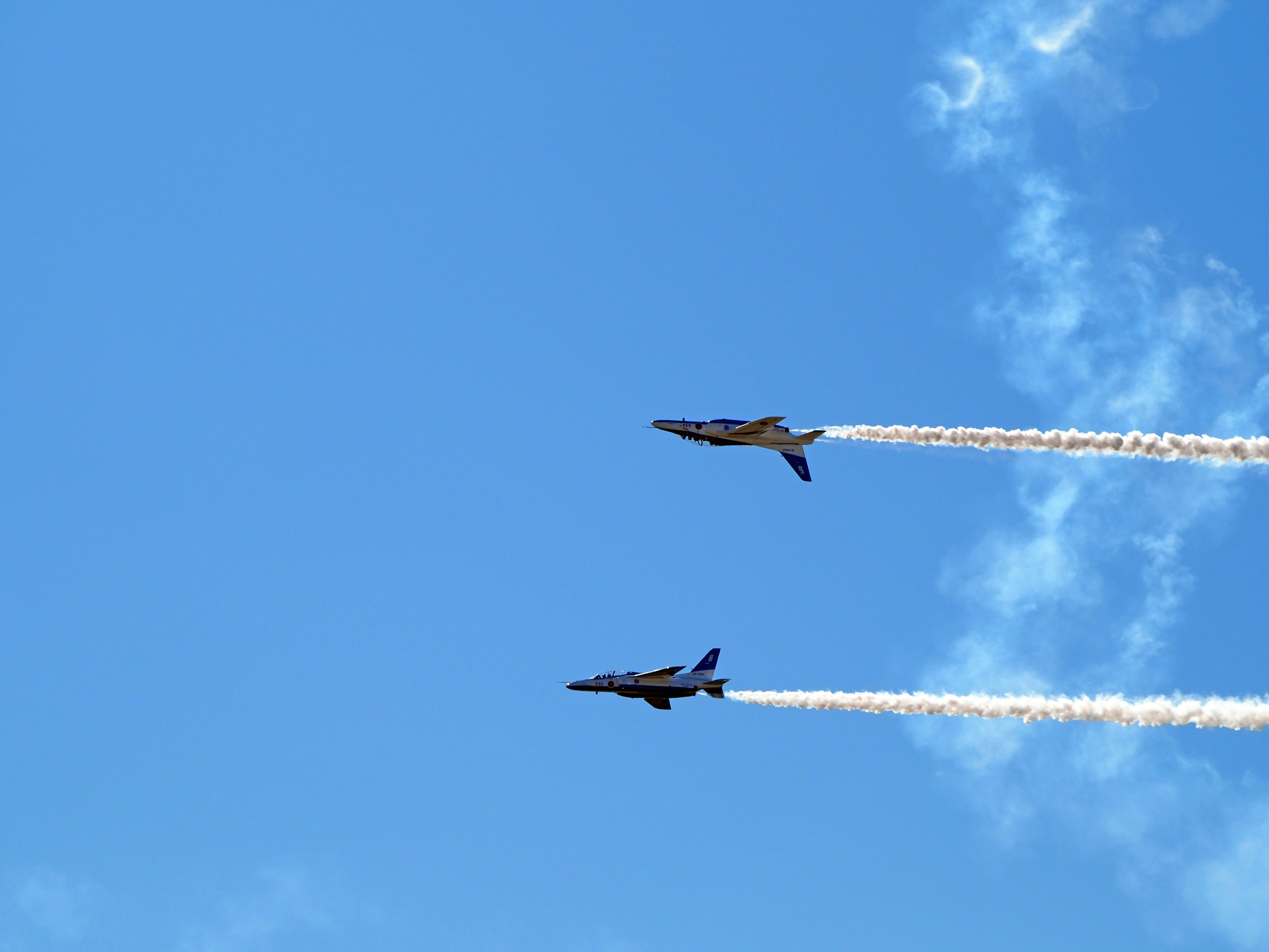 Two fighter jets flying against a blue sky with contrails