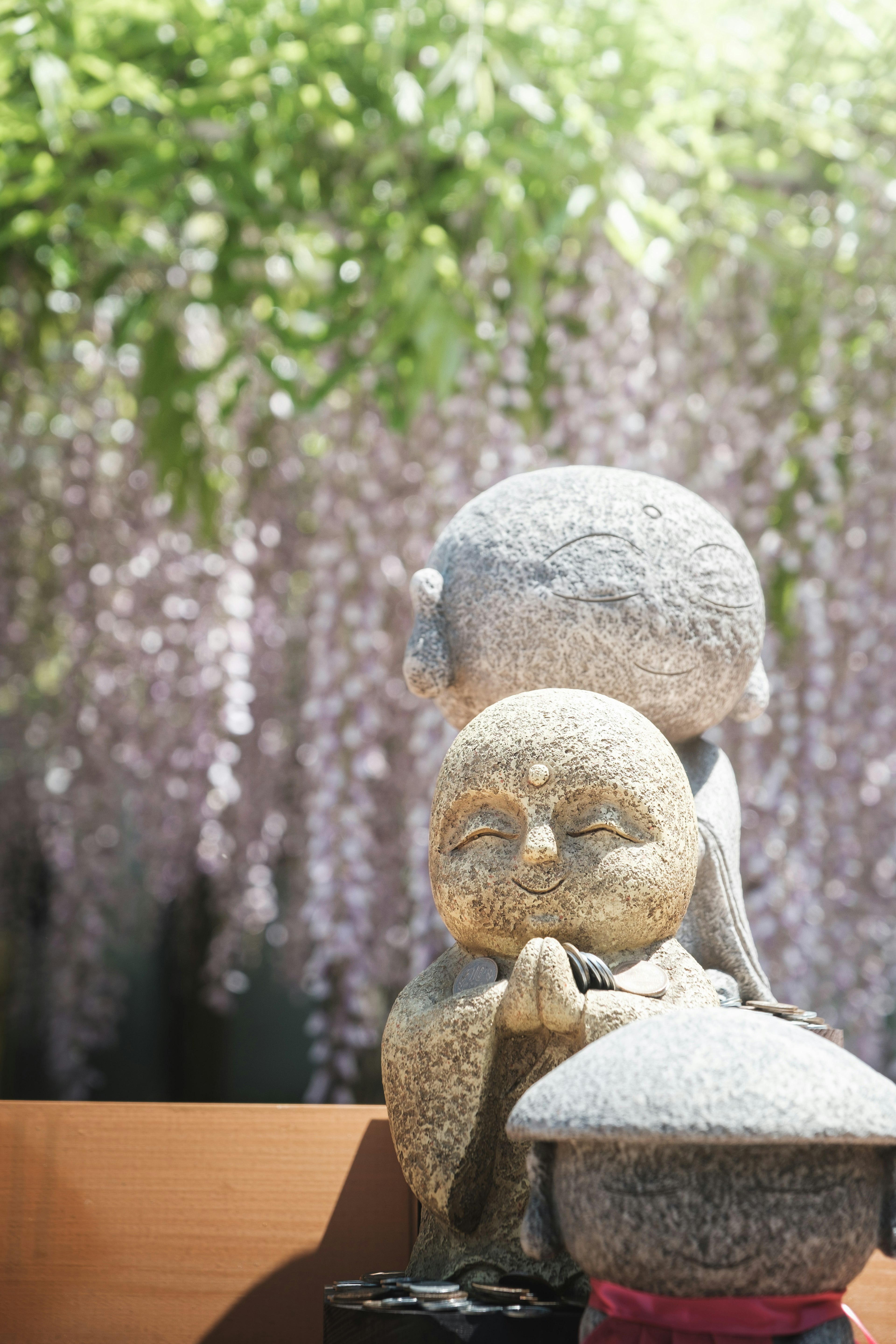 石像の子供と大人が手を合わせて祈る姿 背景には藤の花が咲いている