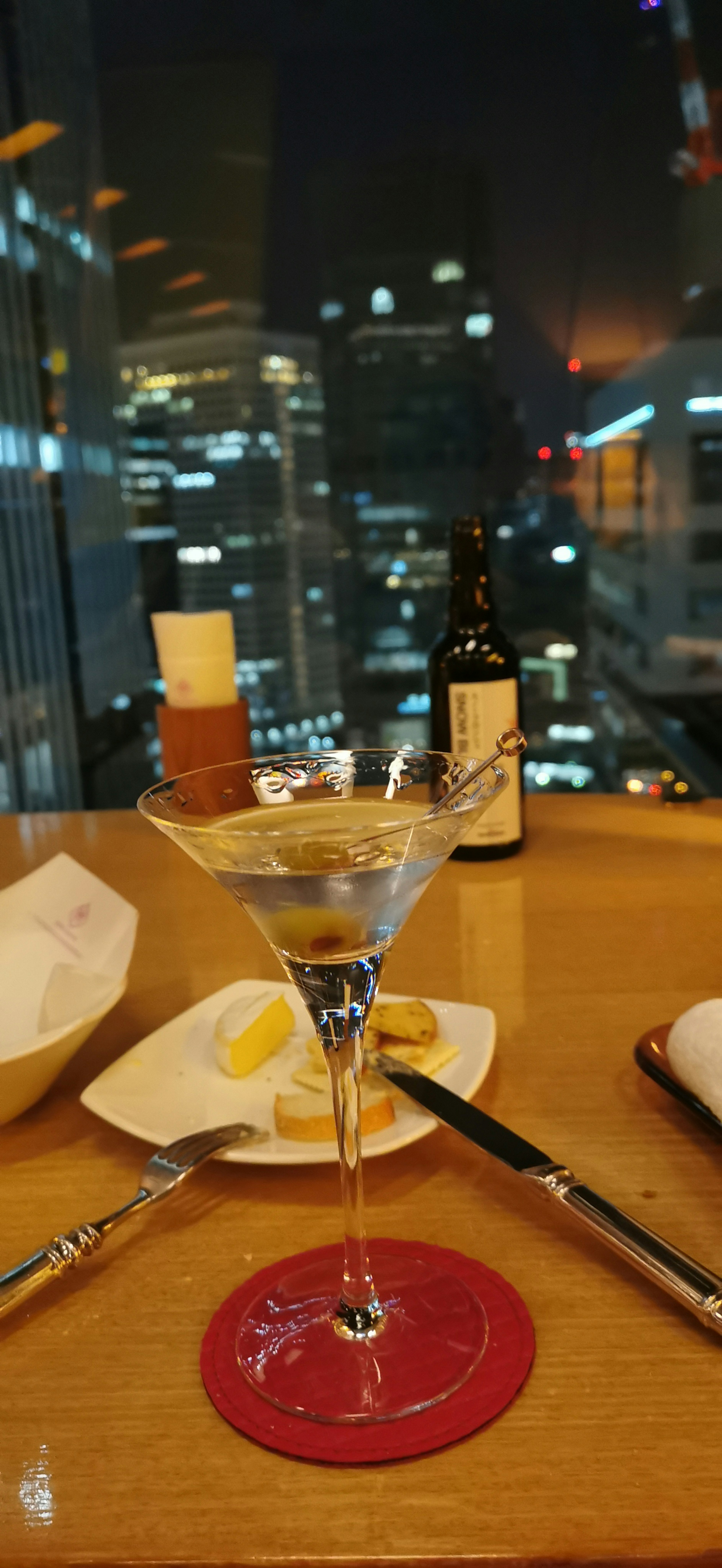 Table setting at a high-end restaurant featuring a cocktail and city skyline