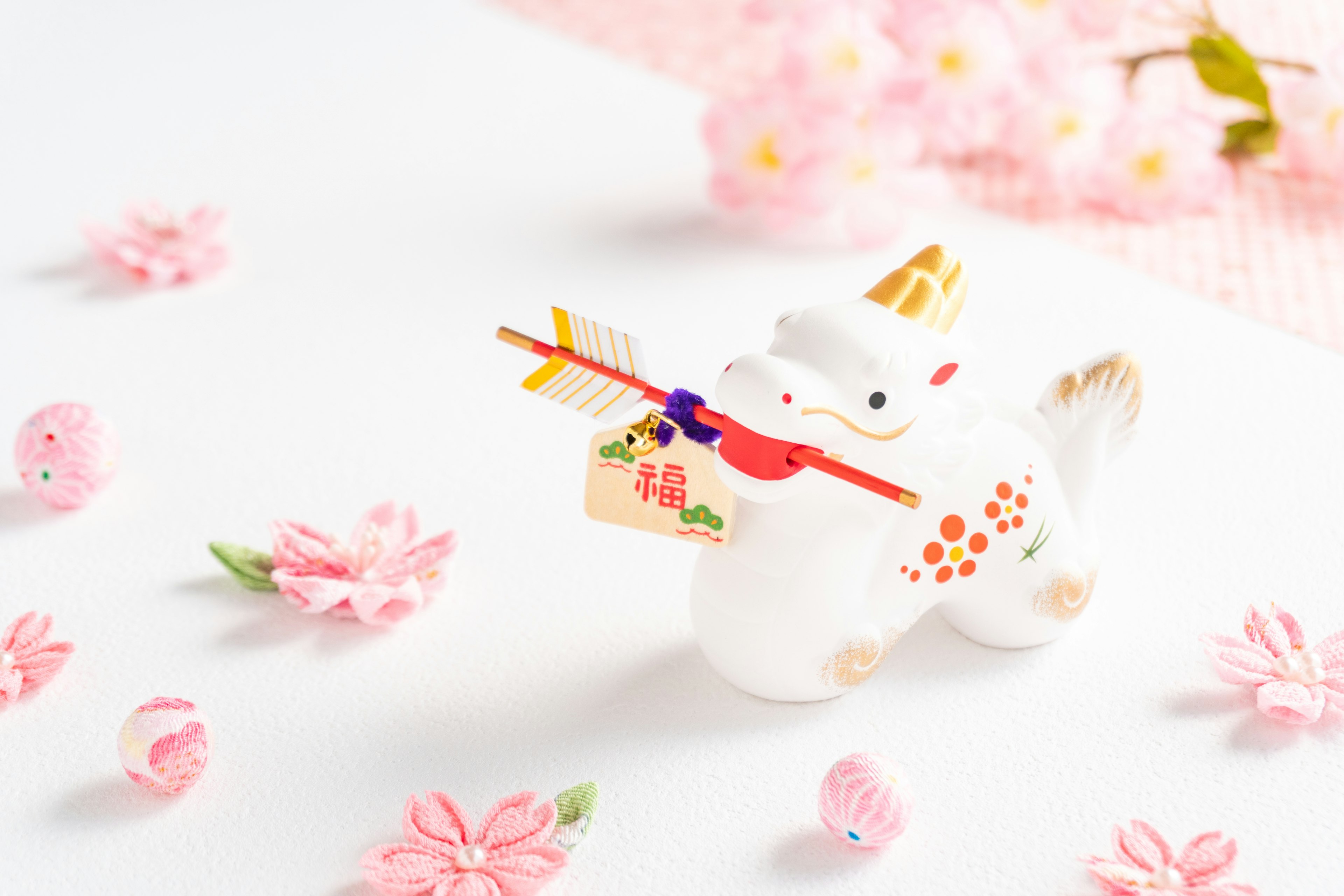 A white lion figurine holding a red bow and arrow surrounded by pink flower petals