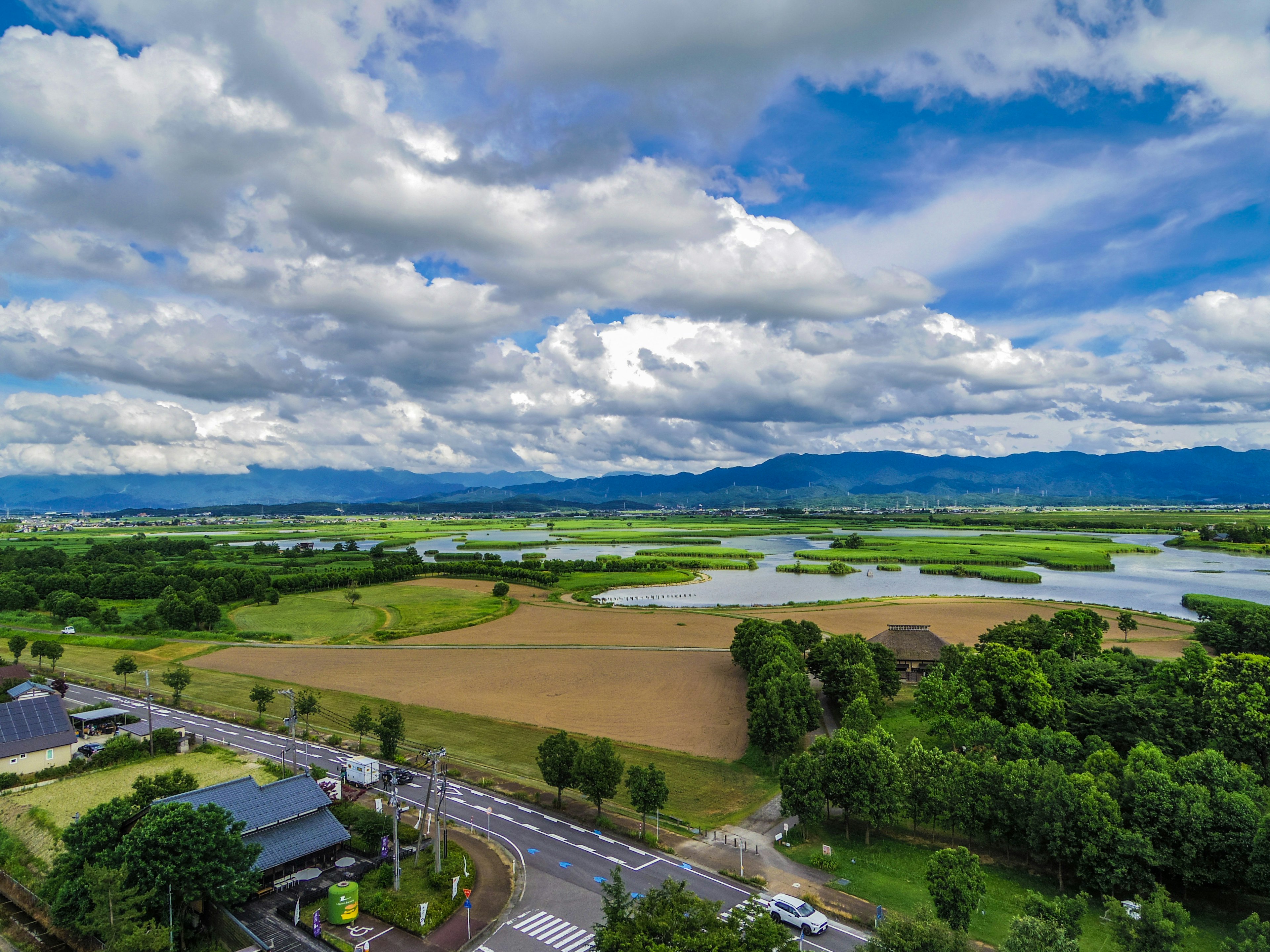 Ampie terre agricole con un fiume che scorre sotto un cielo blu e nuvole