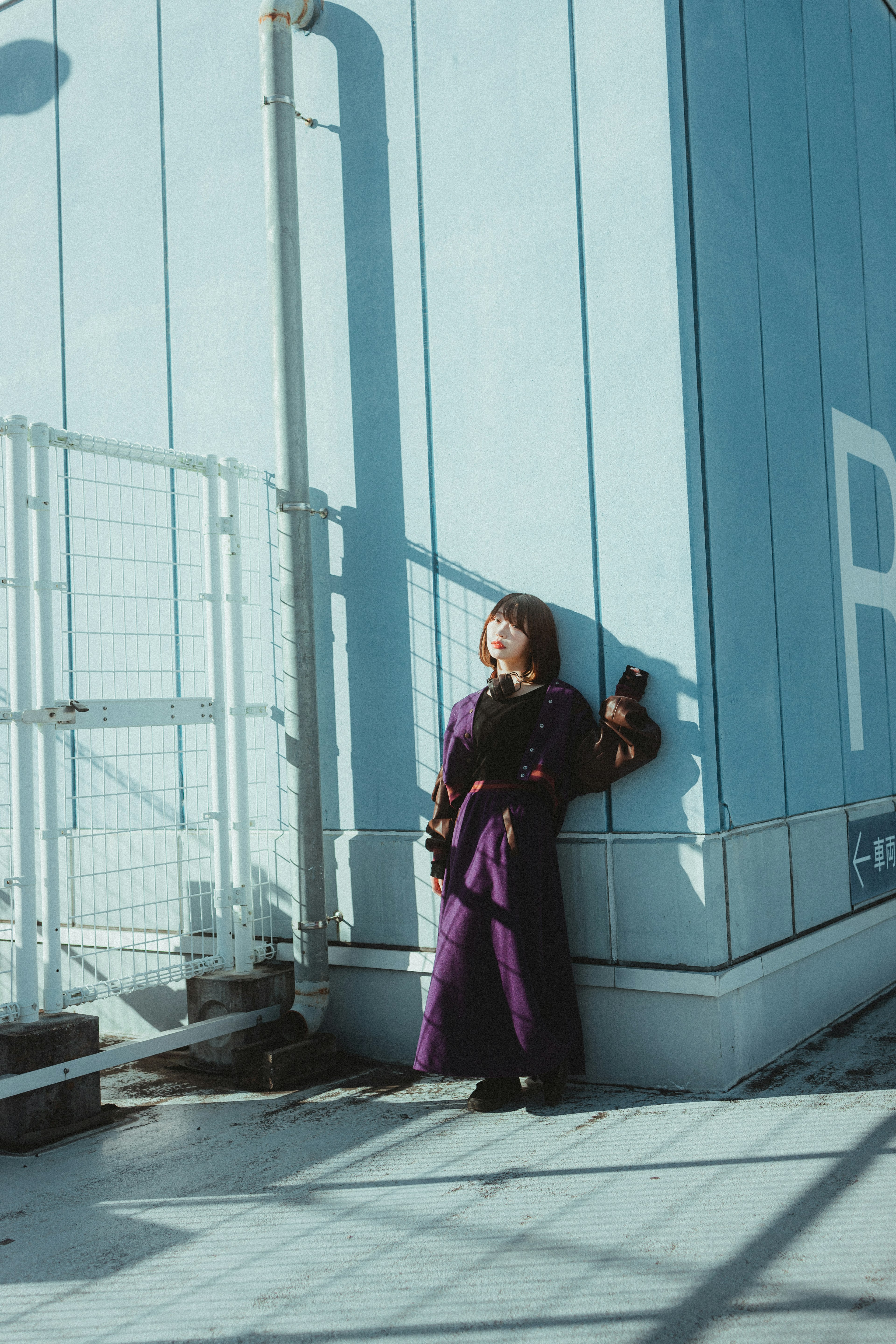 Frau in lila Outfit steht vor einer blauen Wand mit starken Schatten