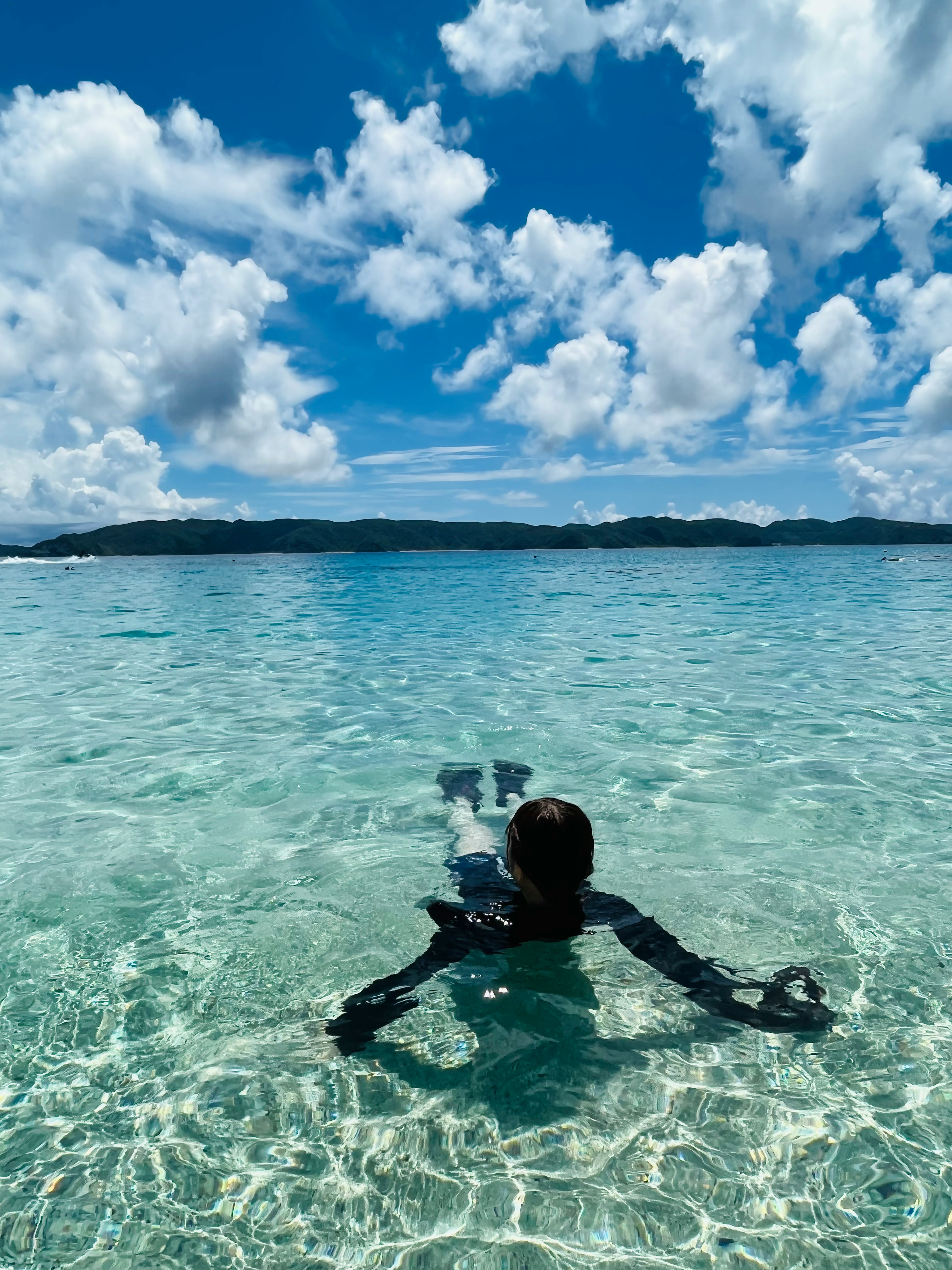 Person schwimmt in klarem Wasser unter blauem Himmel