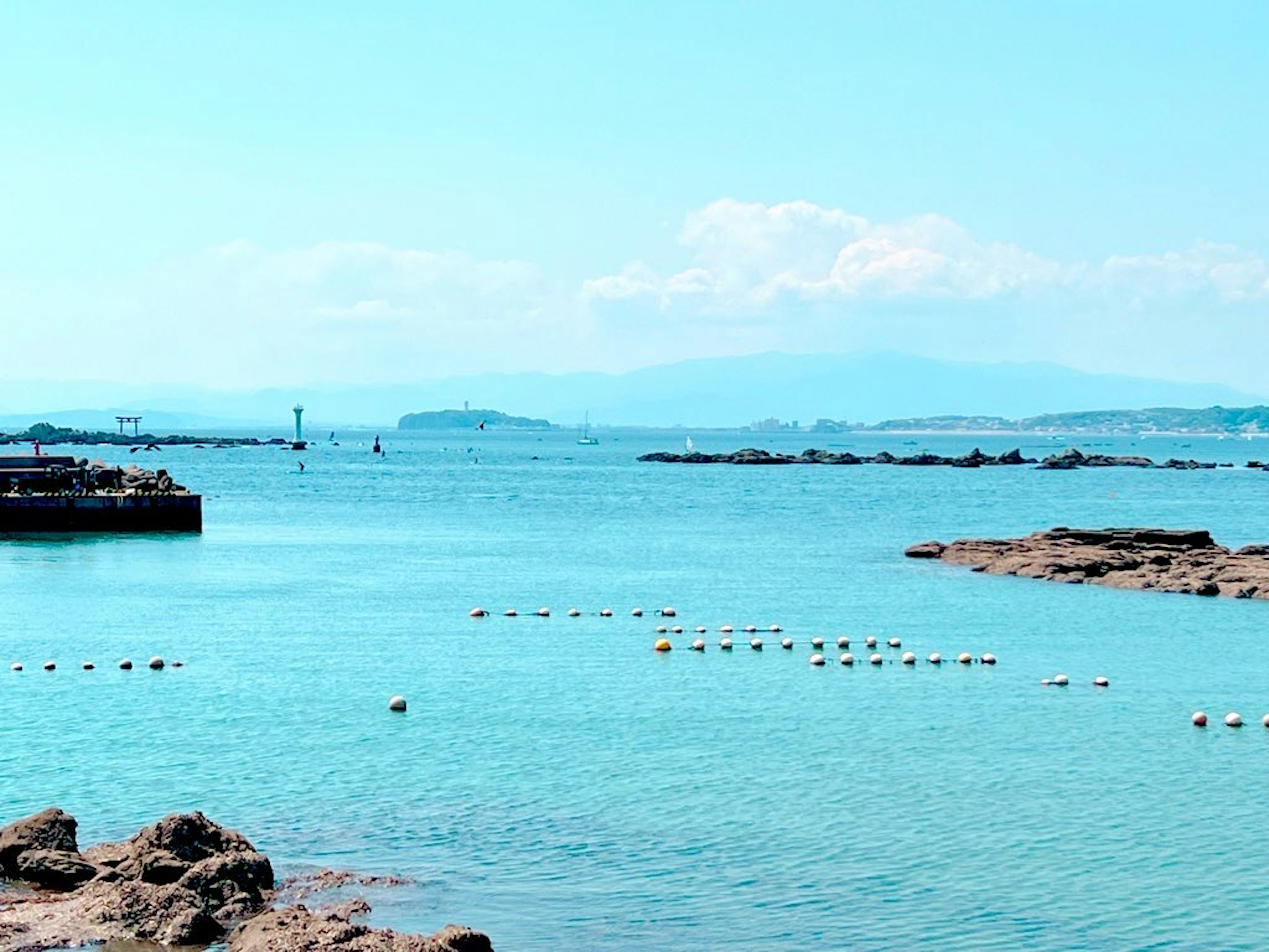 Vista escénica de un mar azul con una costa rocosa y boyas flotantes en agua clara