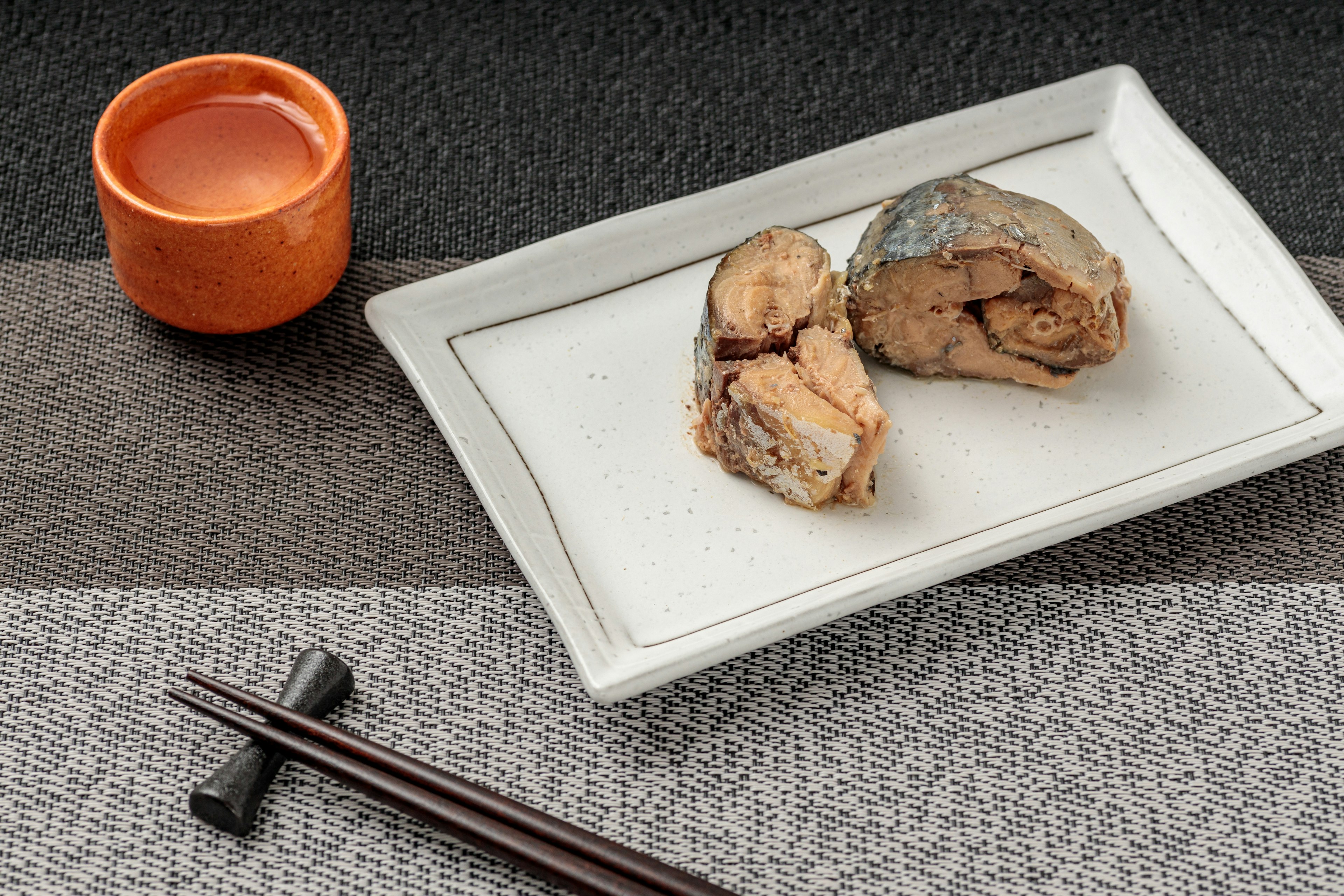 Plat de poisson servi sur une assiette blanche avec une petite tasse orange de boisson