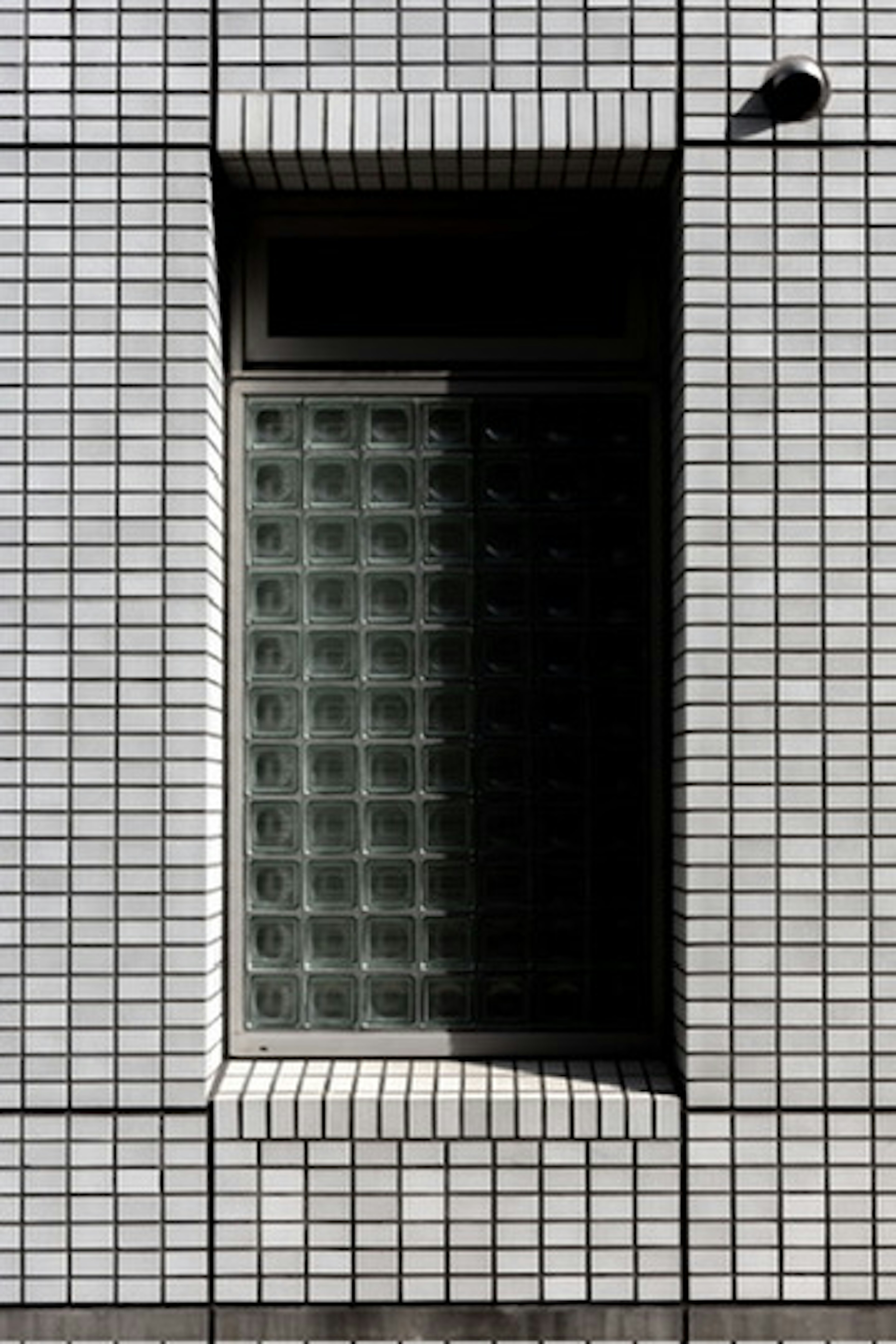 Ventana de bloques de vidrio enmarcada por una pared de azulejos blancos