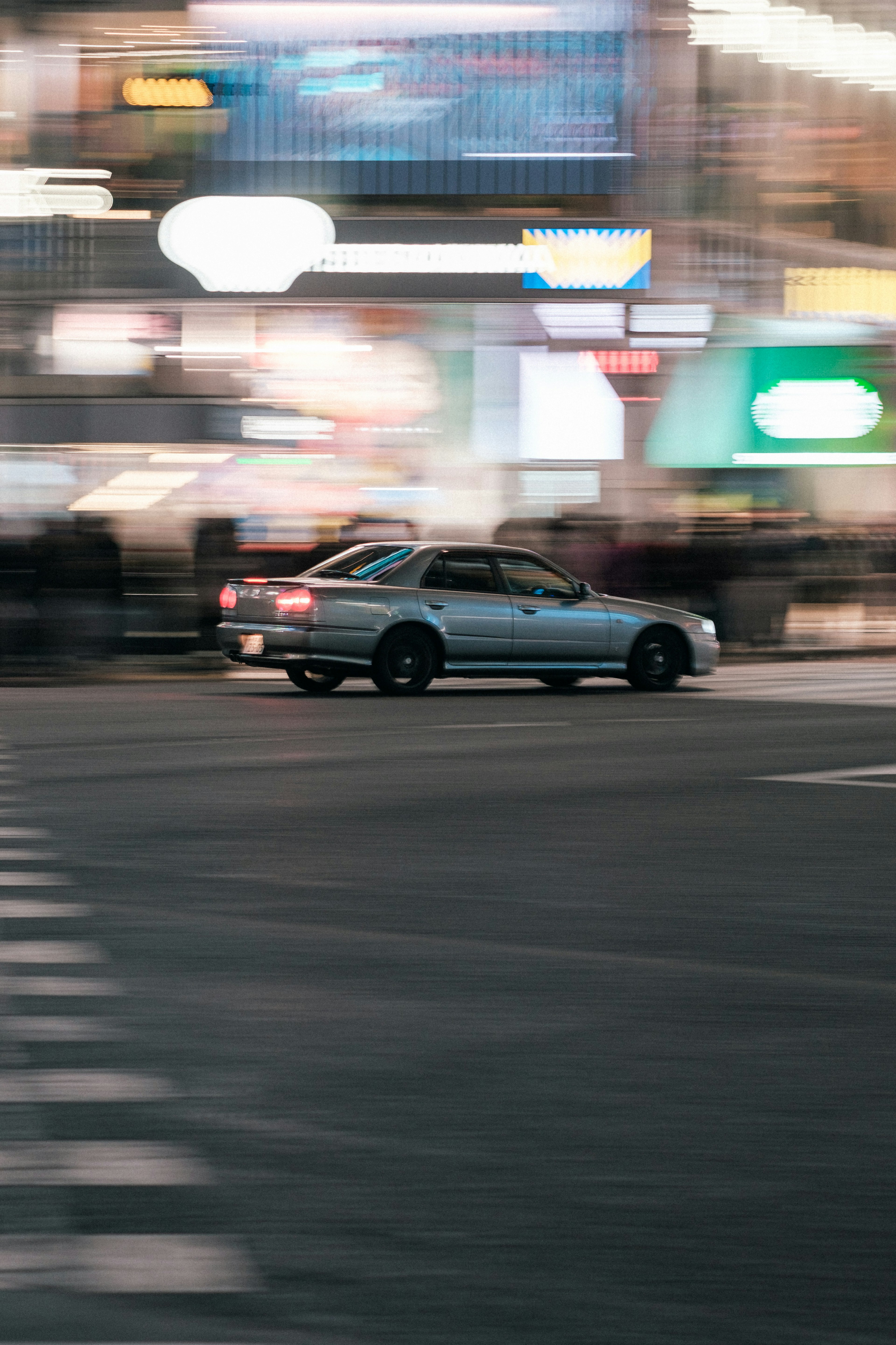 Silver car turning at a busy intersection with blurred lights