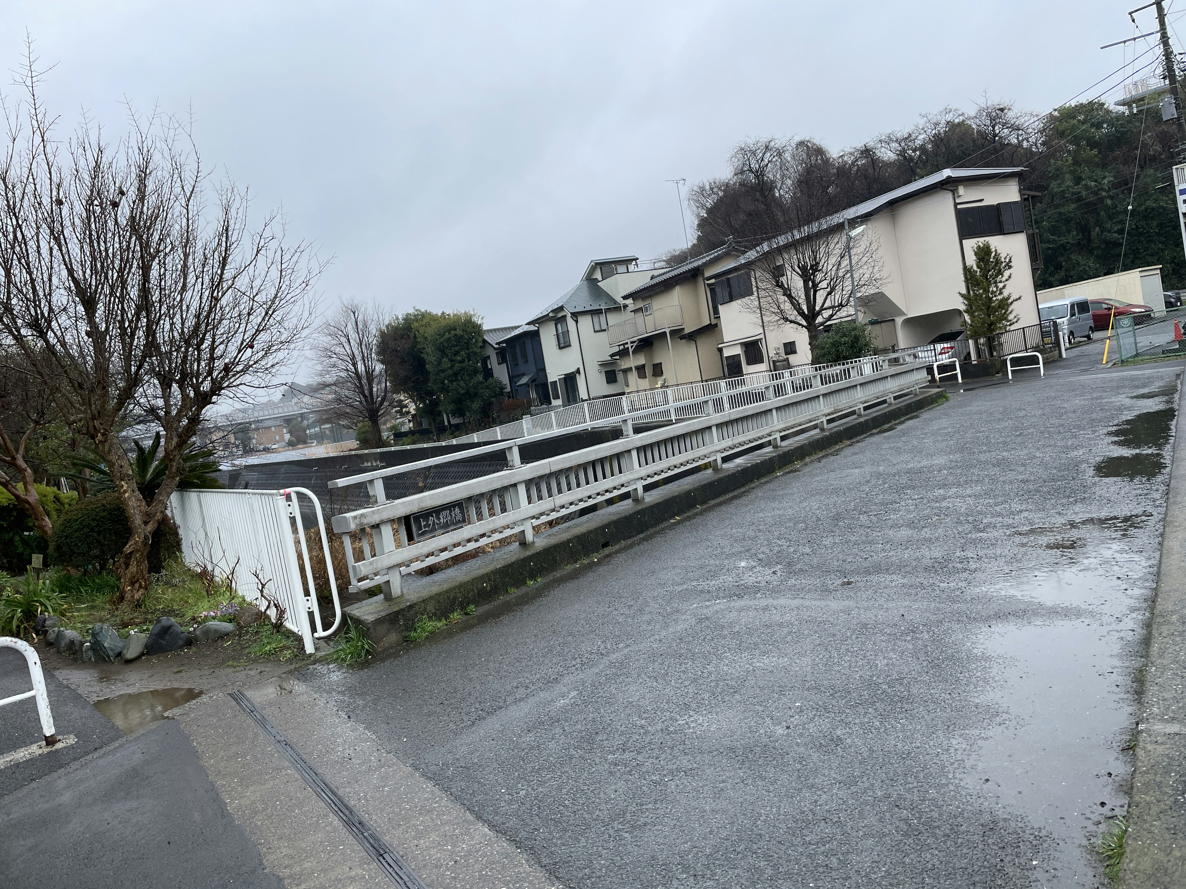 雨の降る道路と住宅街の風景 橋と木々が見える