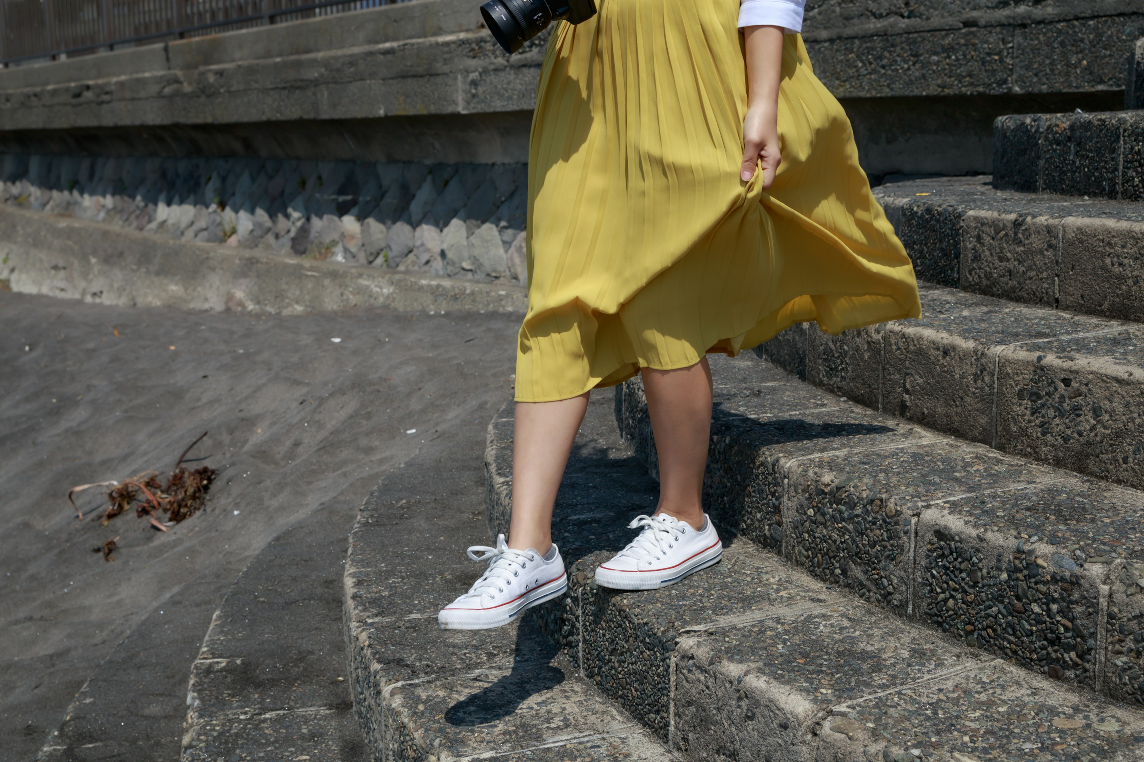 A woman wearing a yellow skirt descending stairs holding a camera