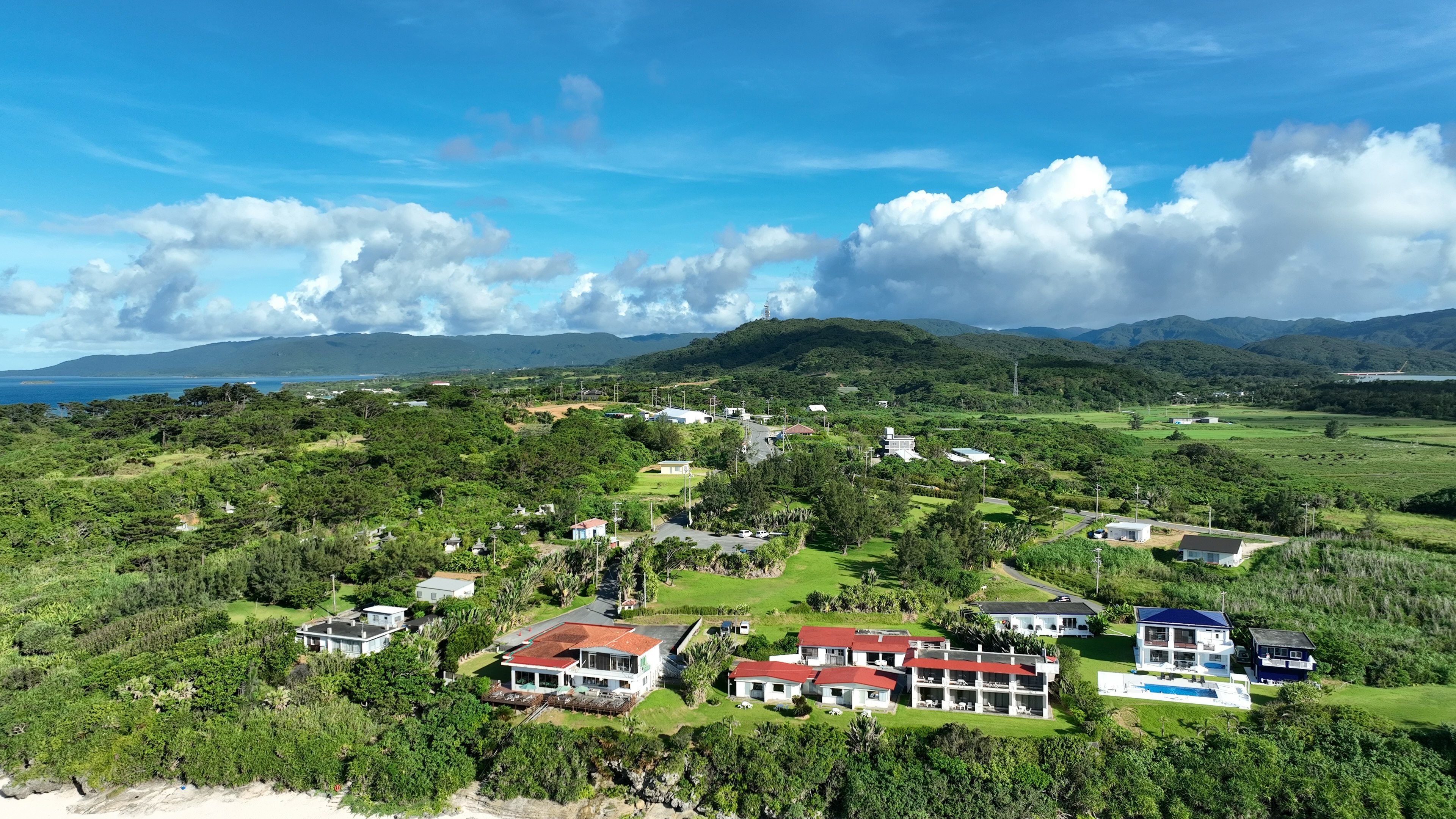 Aerial view of lush green landscape with scattered houses under a blue sky