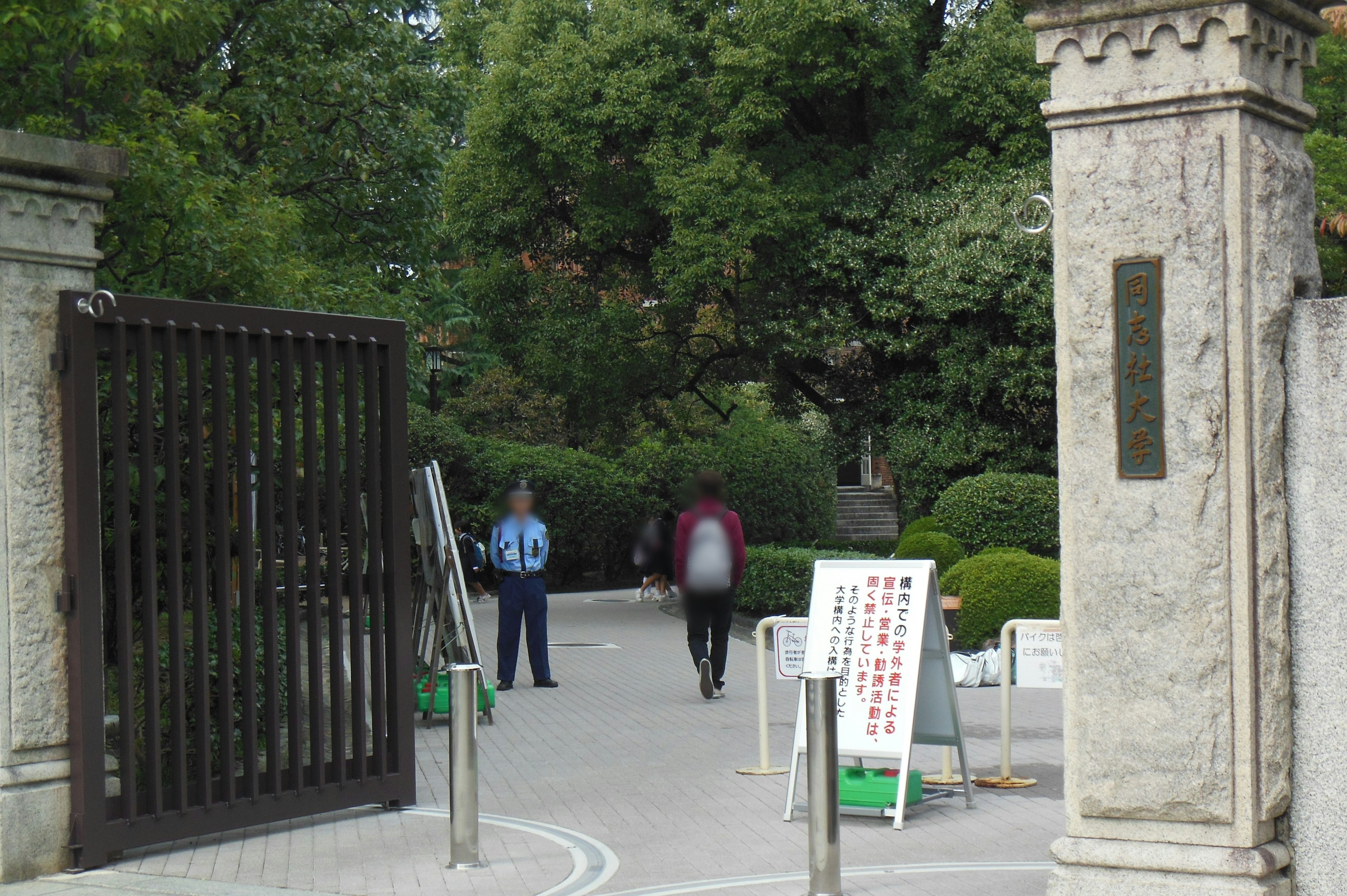 公園の入口に立つ二人の人物と緑豊かな背景