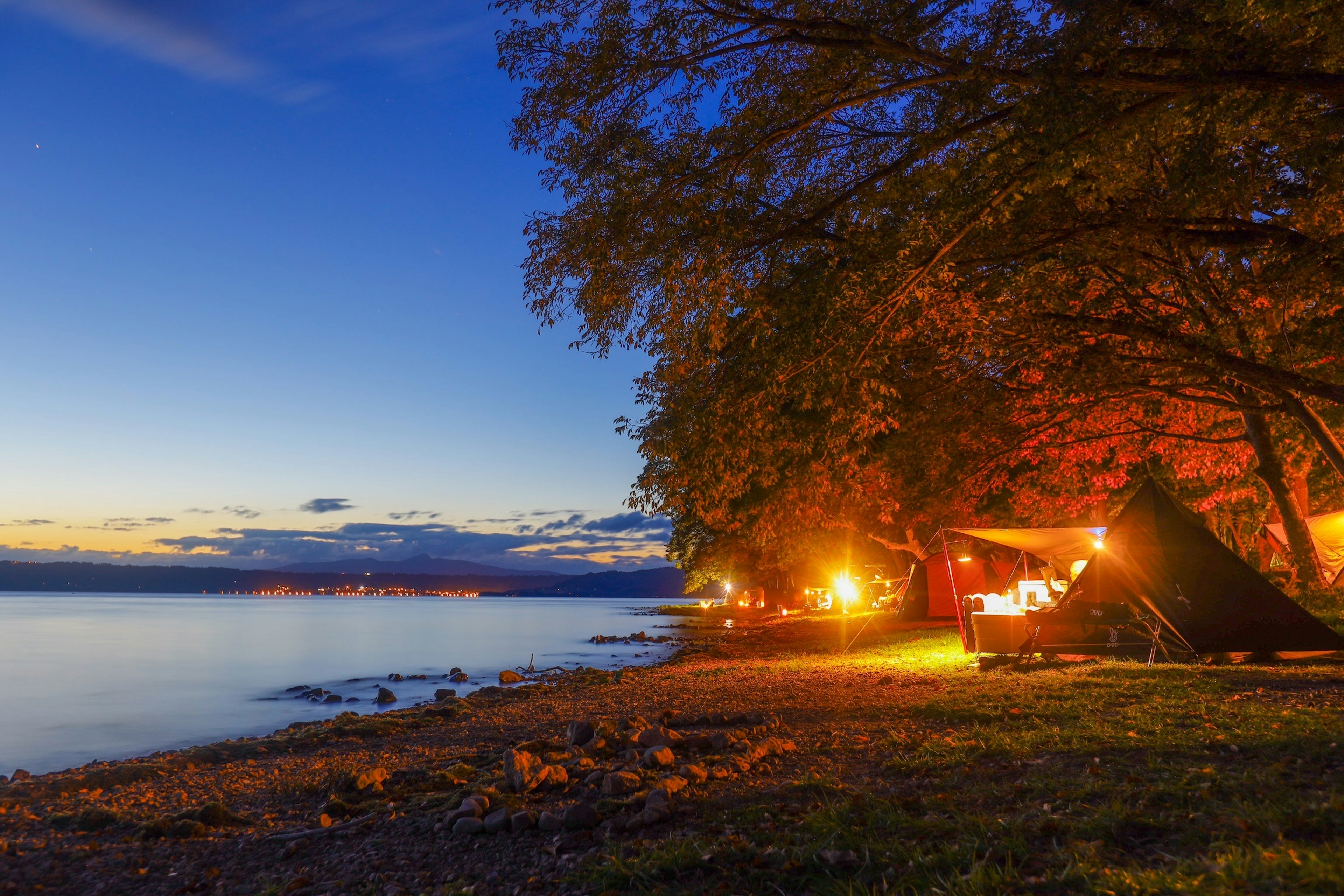 Camping tranquilo junto al lago al anochecer lámparas brillantes y árboles iluminados