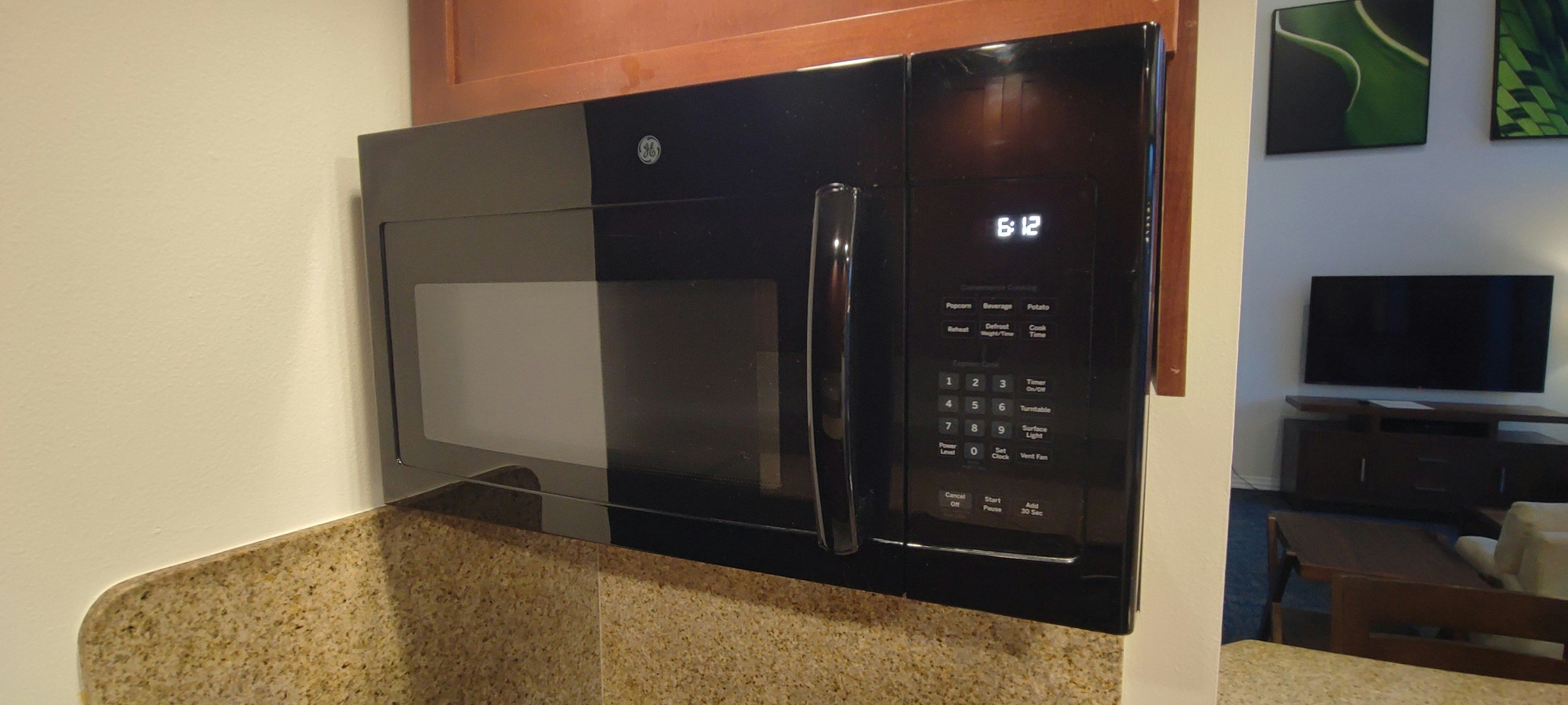 Black microwave mounted in a kitchen with a granite countertop