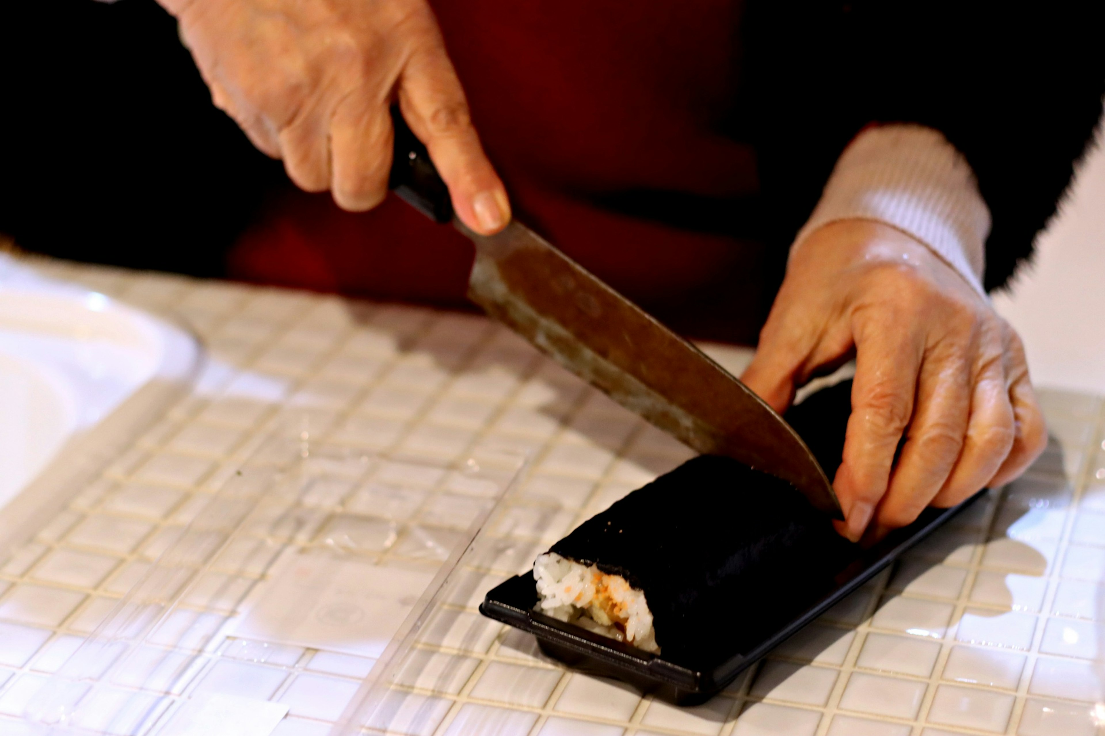 Close-up of hands cutting sushi with a knife on a black plate