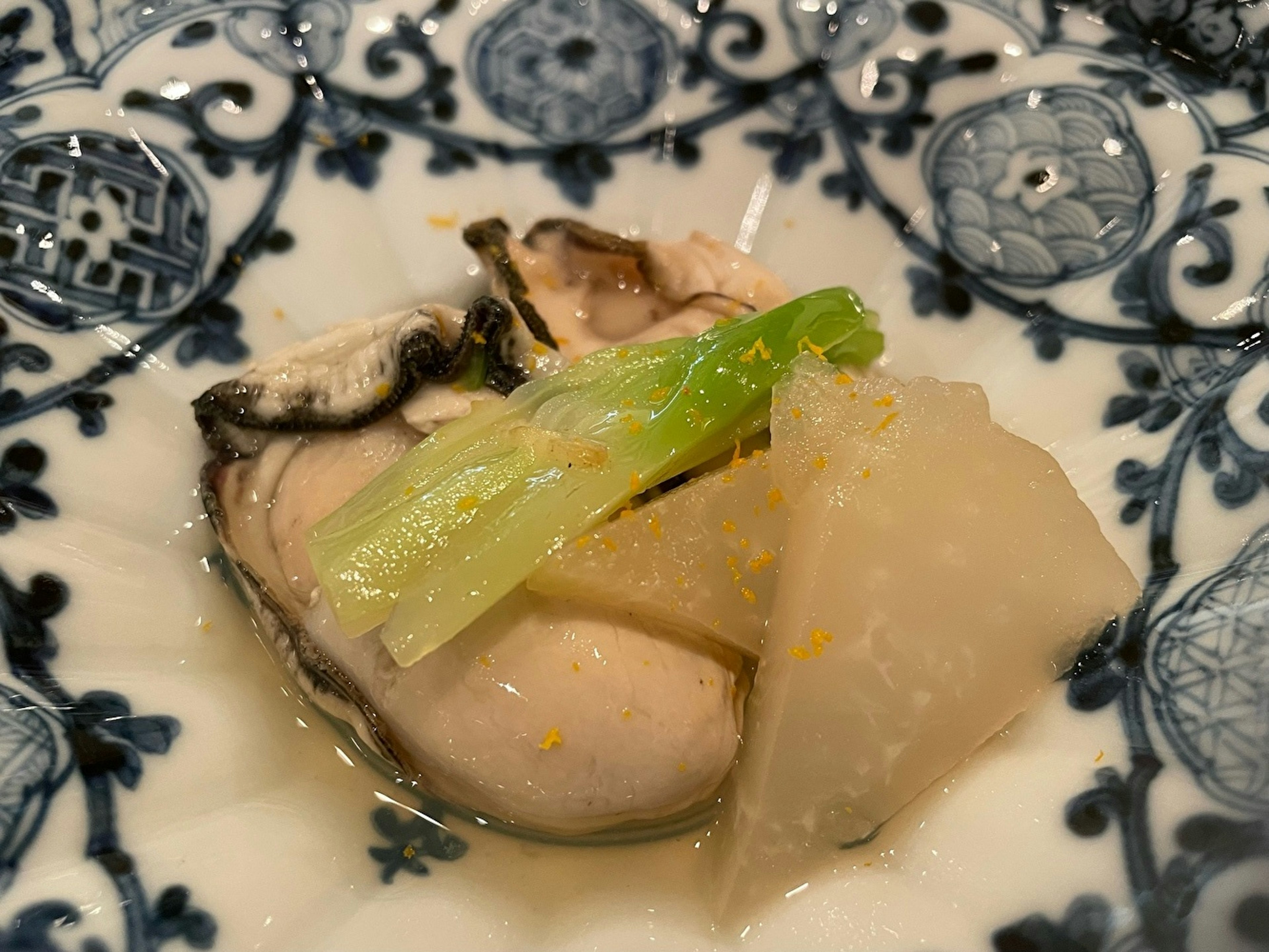 Fresh oyster served on a decorative blue and white plate with slices of daikon and green onion