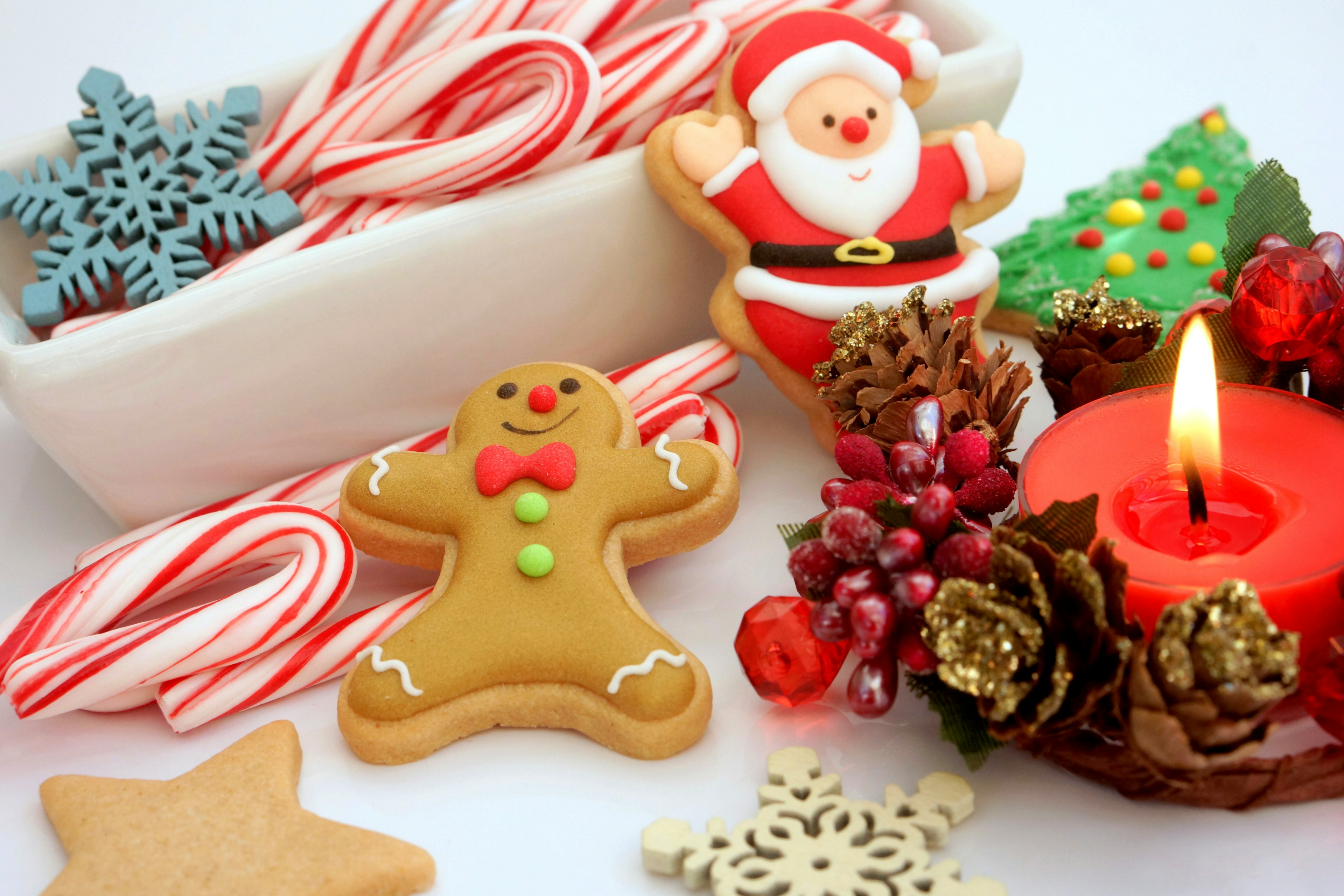 Eine festliche Anordnung mit einem Weihnachtsmann-Keks einem Lebkuchenmann Zuckerstangen einer roten Kerze und Tannenzapfen auf einem Tisch