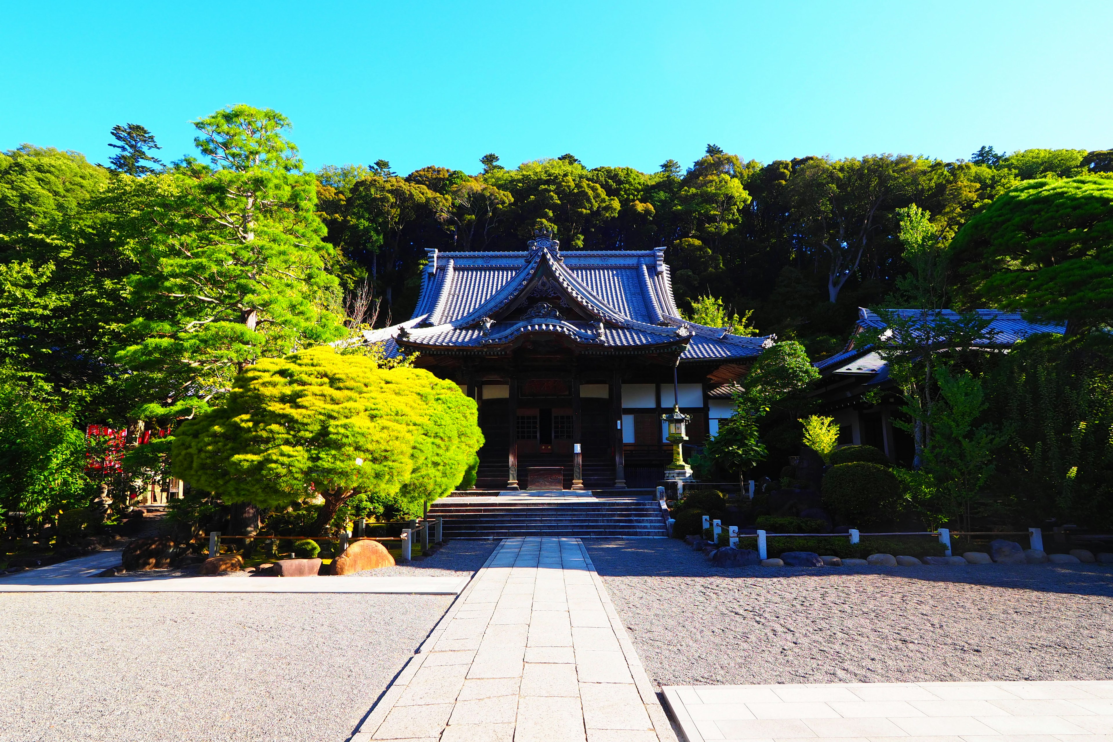 Traditioneller japanischer Tempel umgeben von üppigem Grün und einem Steinweg