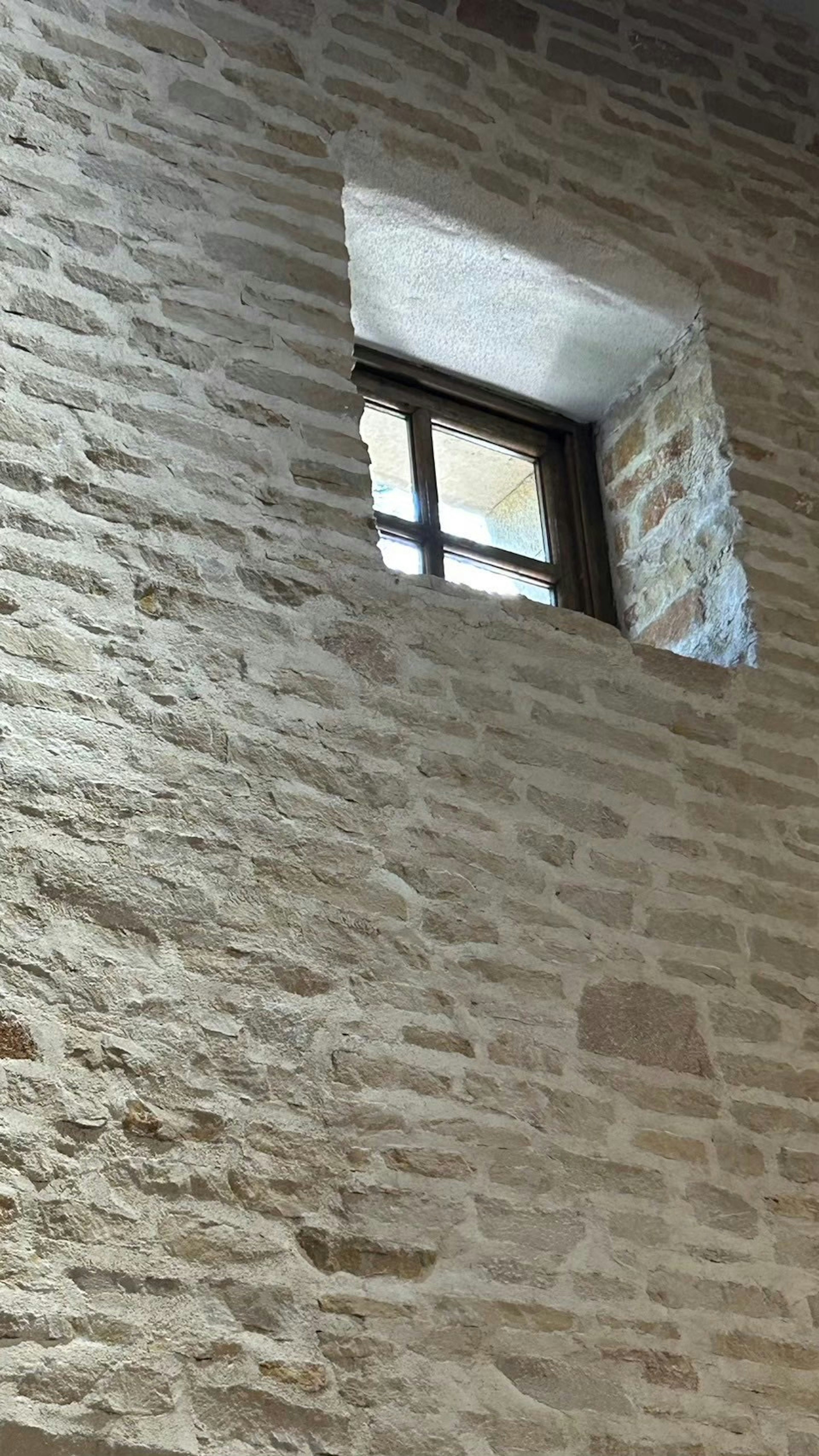 Interno di una stanza luminosa con una piccola finestra in un muro di pietra