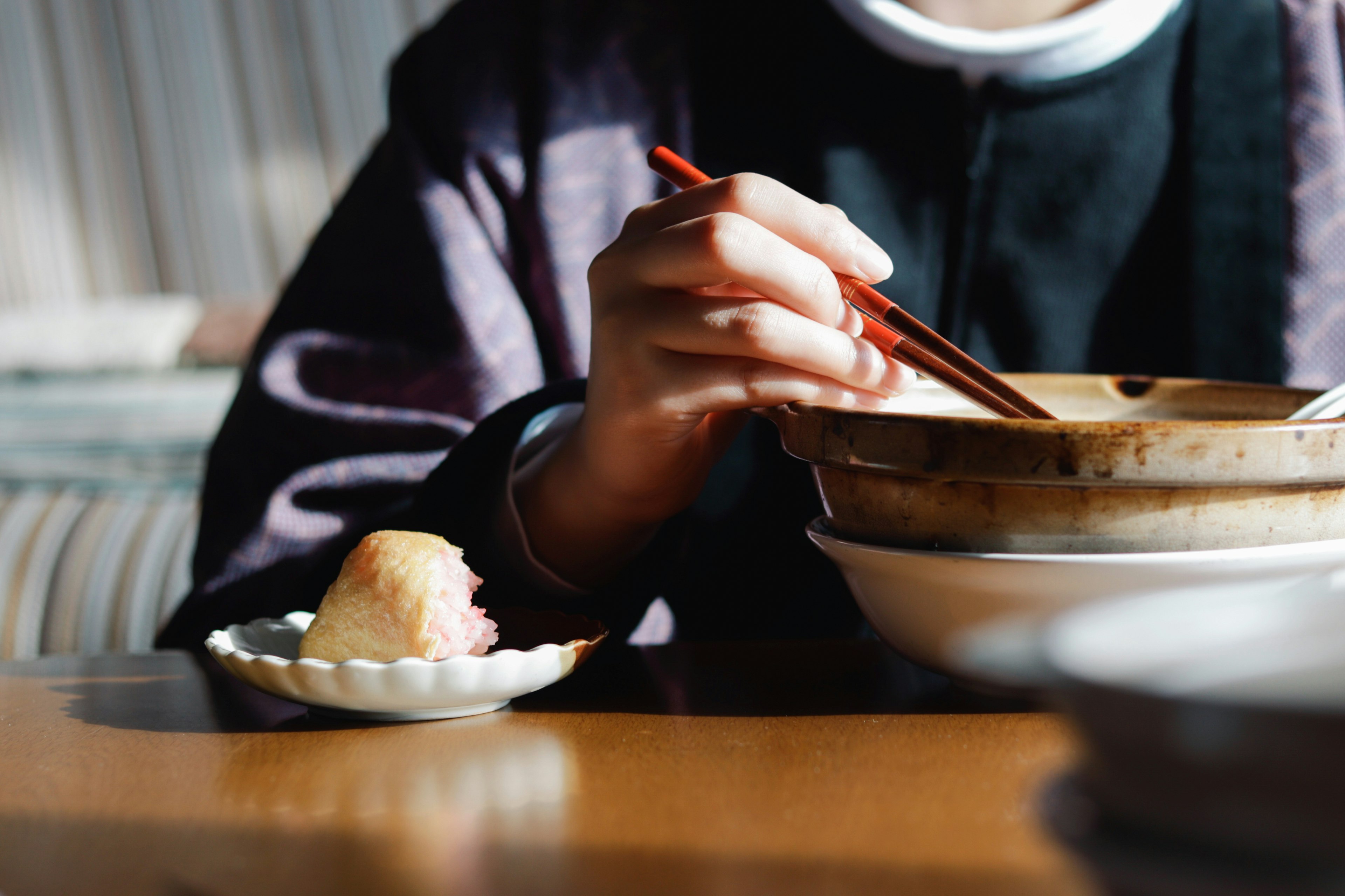 手用筷子吃碗里的食物，旁边有一个小盘子