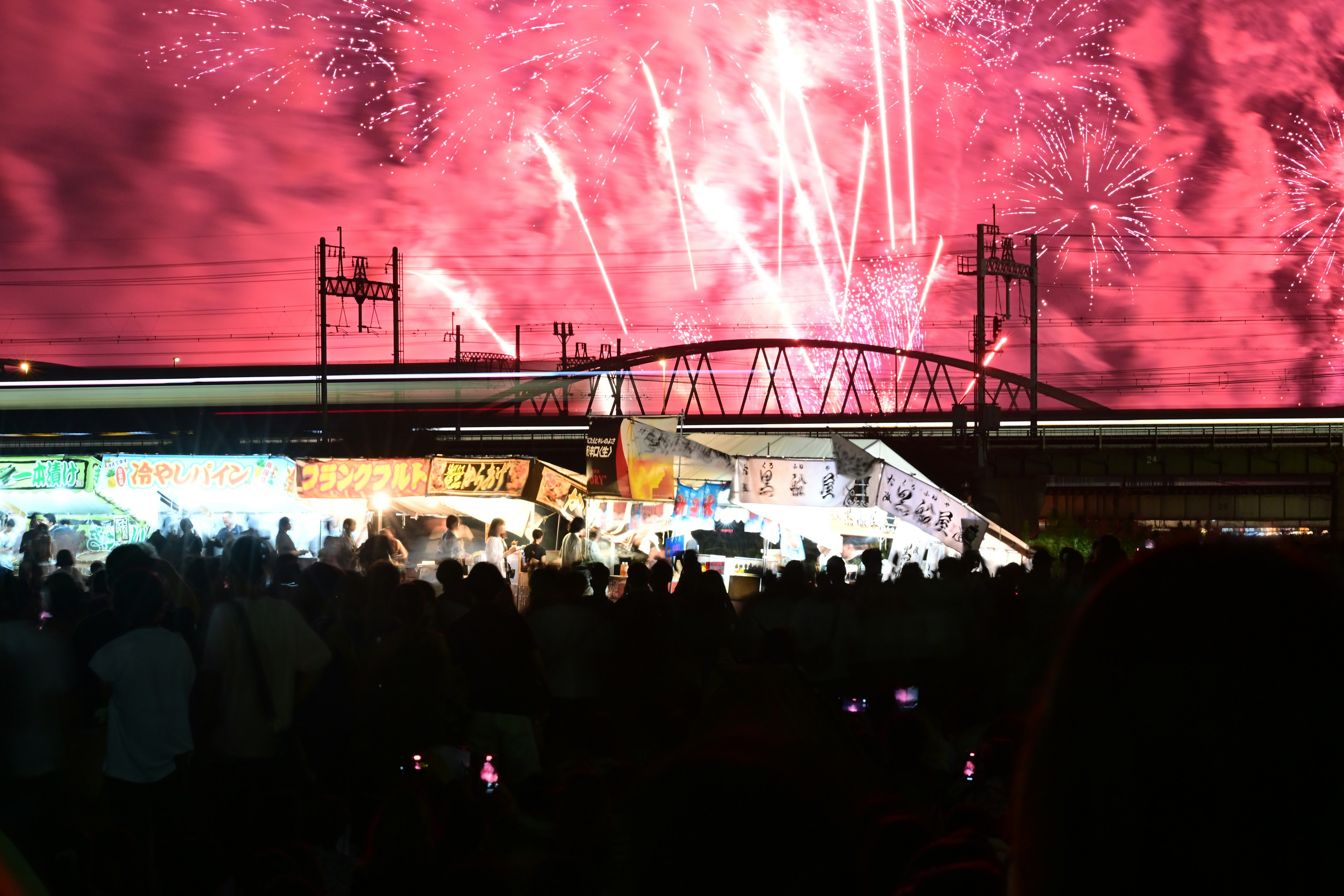 I fuochi d'artificio illuminano il cielo notturno sopra un ponte e una folla