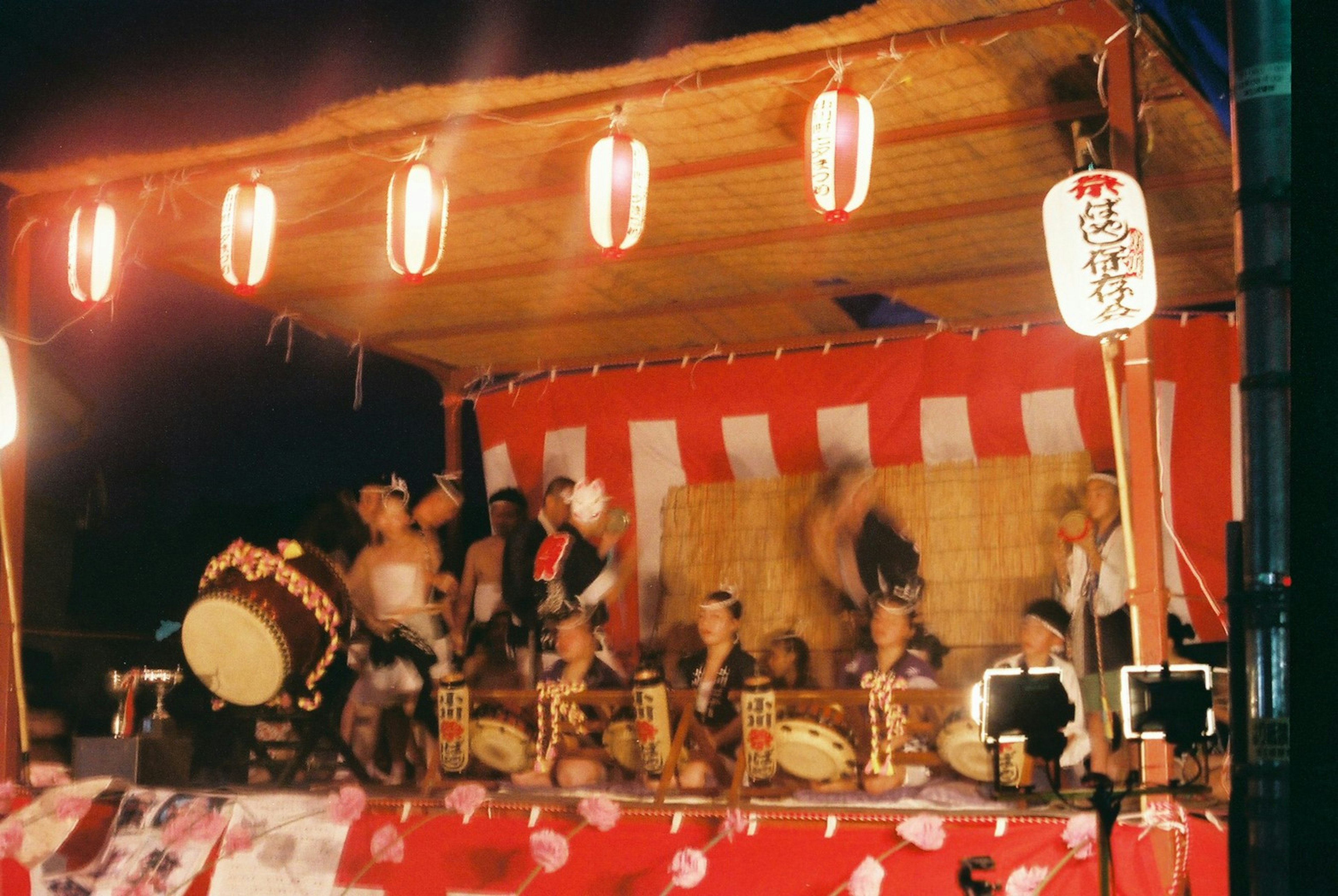 Pertunjukan drum tradisional di stan festival dengan lentera di latar belakang pada malam hari