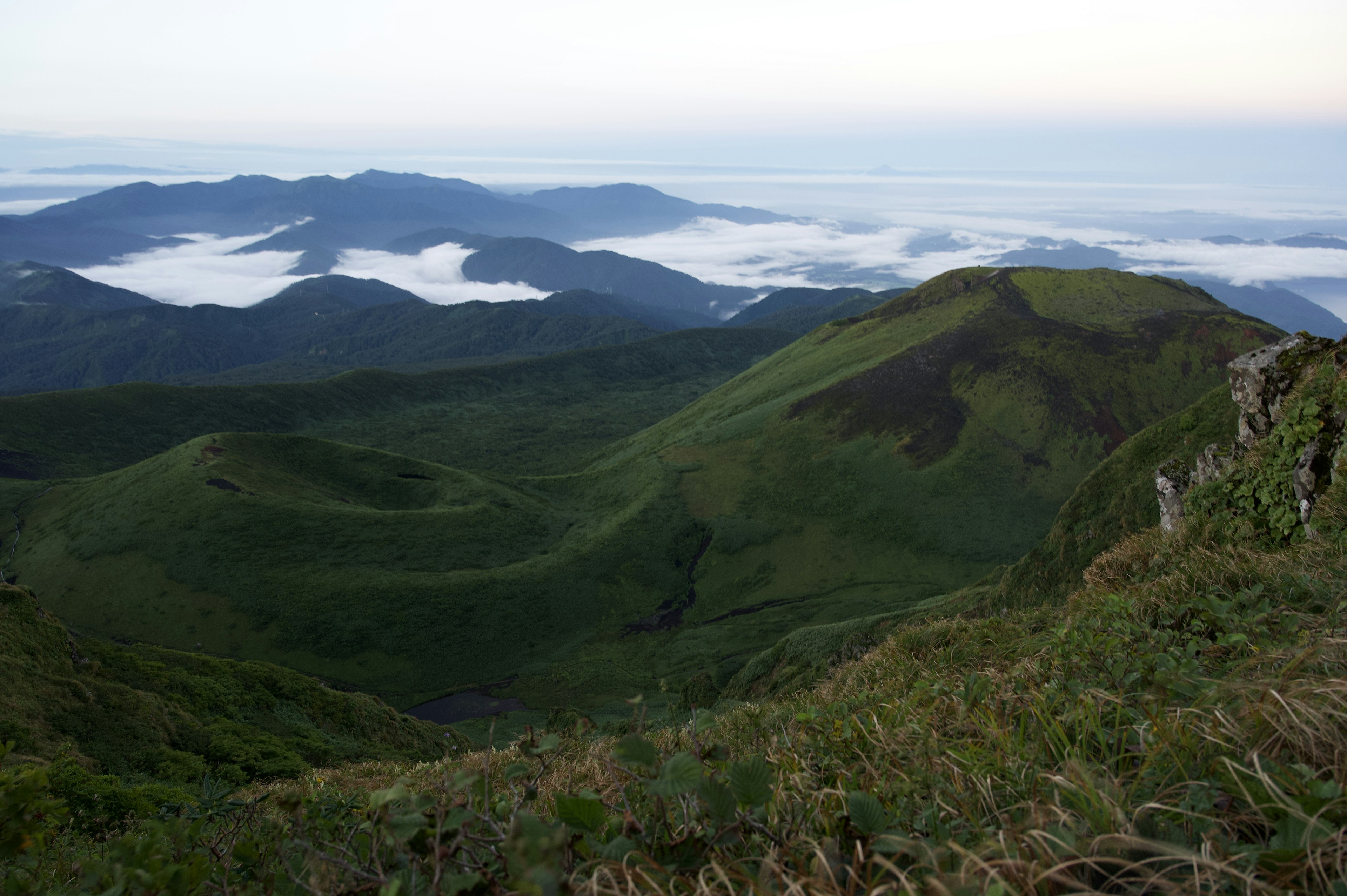 Perbukitan hijau subur dengan lautan awan di latar belakang